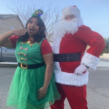 Woman in elf costume and Santa Claus pose together outside on a sunny day.