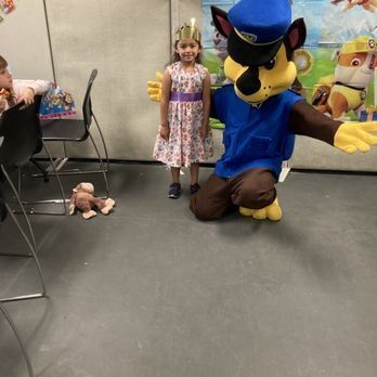 Girl in dress and Chase the Paw Patrol character pose together at party.