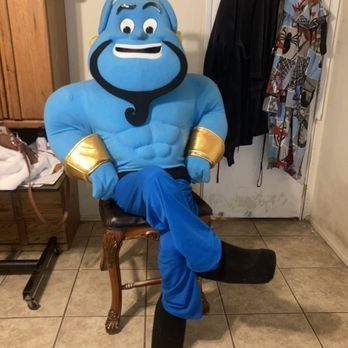 Blue Genie mascot sitting on a wooden chair, wearing blue pants and black boots.