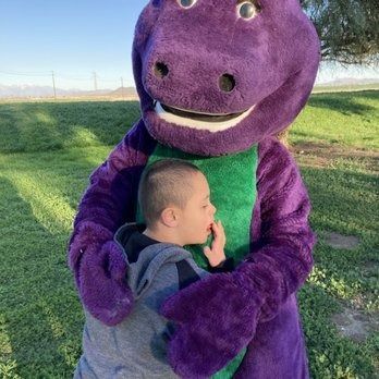 Boy with Down syndrome hugs Barney the dinosaur in an outdoor setting.