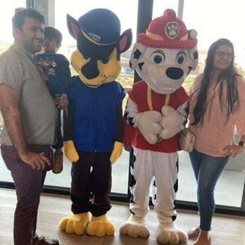A family poses with Chase and Marshall from Paw Patrol. Indoor setting, sunny.