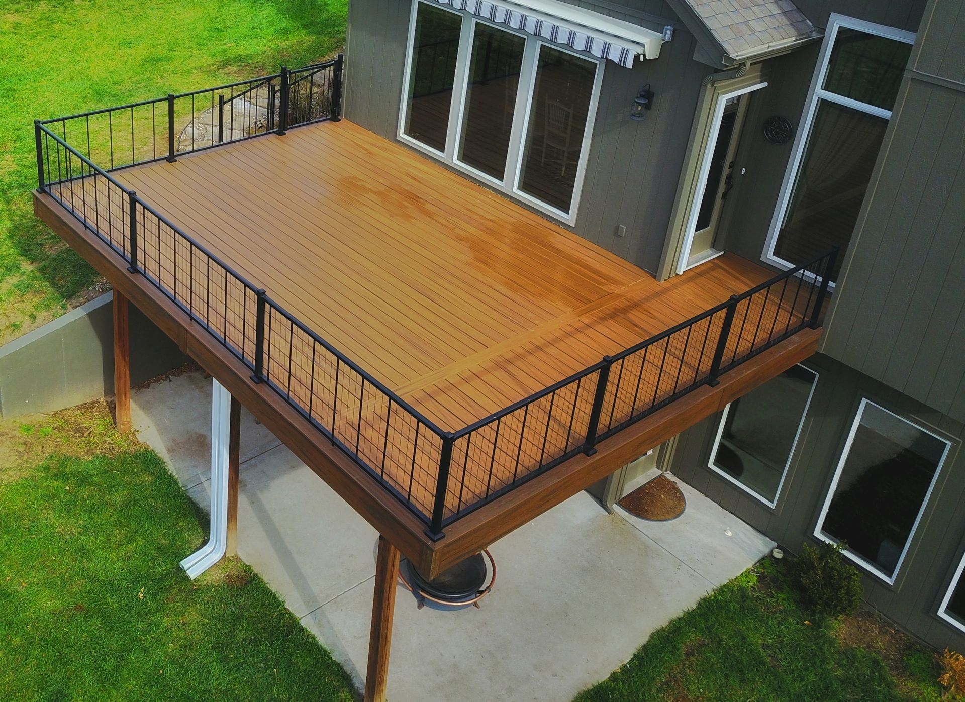 Large wooden deck with black railing attached to a house, overlooking a green yard.