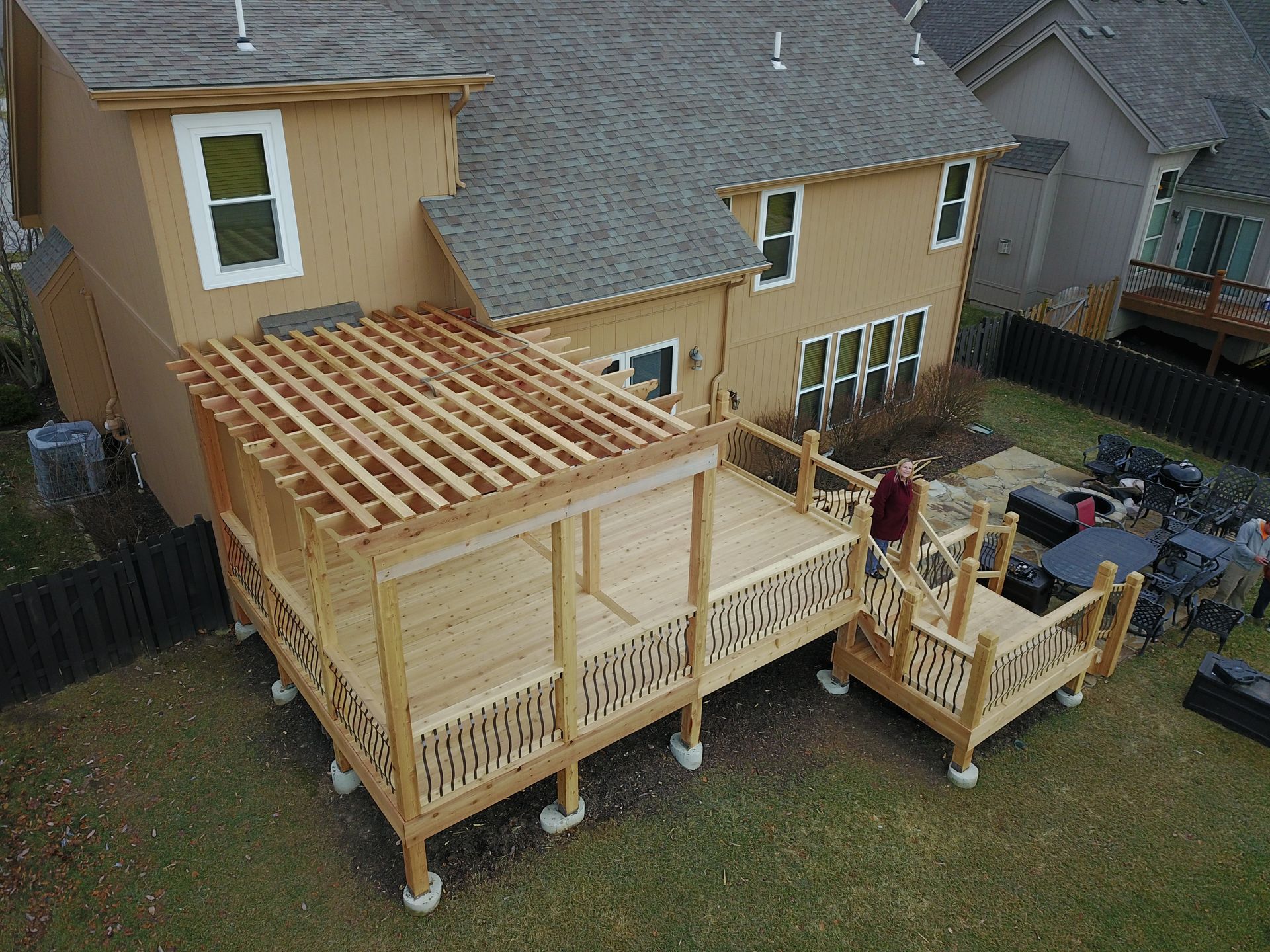 Backyard wooden deck under construction beside a tan house, with a pergola frame and steps.