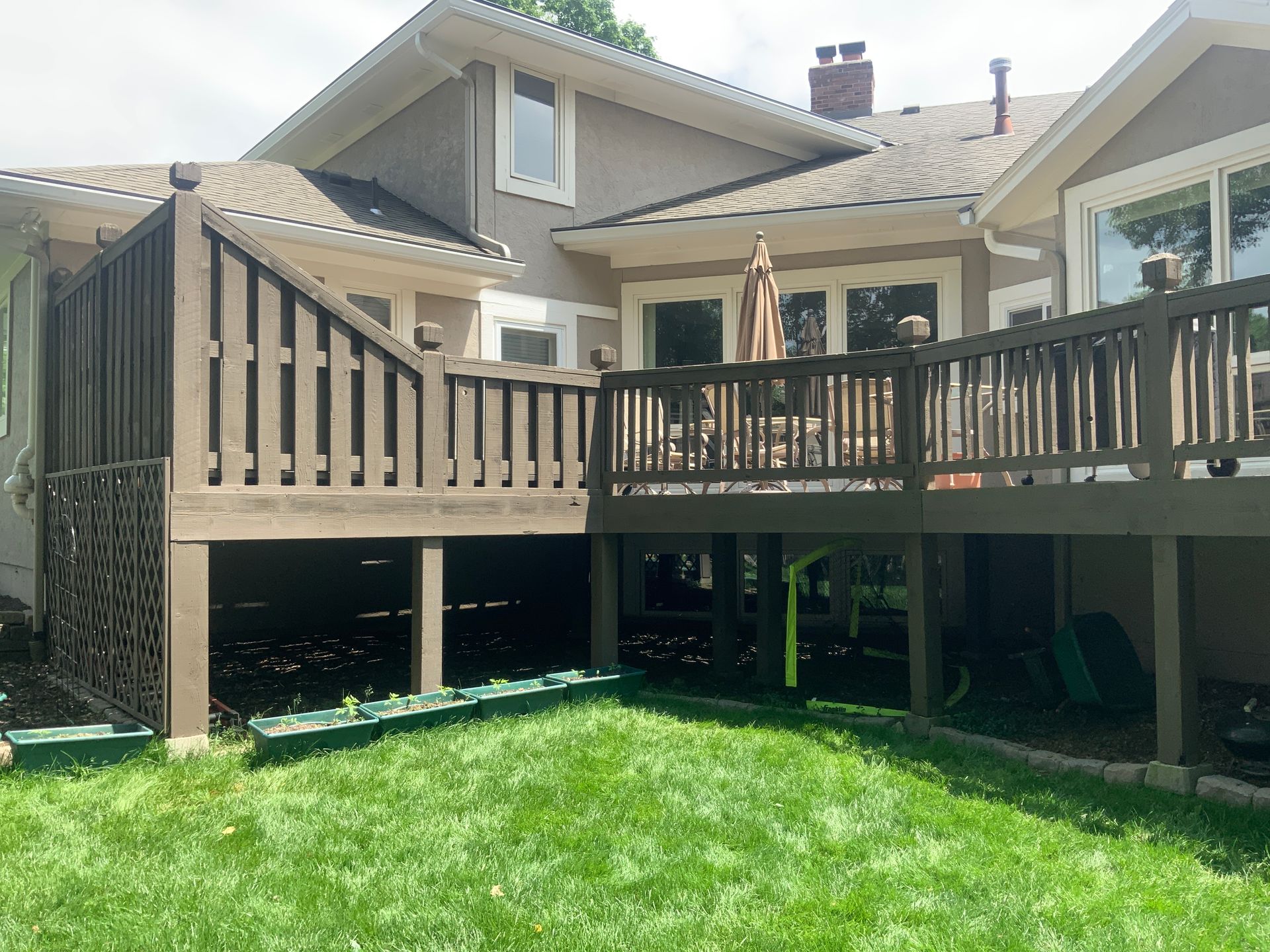 Backyard deck with wooden railings and stairs above a green lawn, attached to a house.