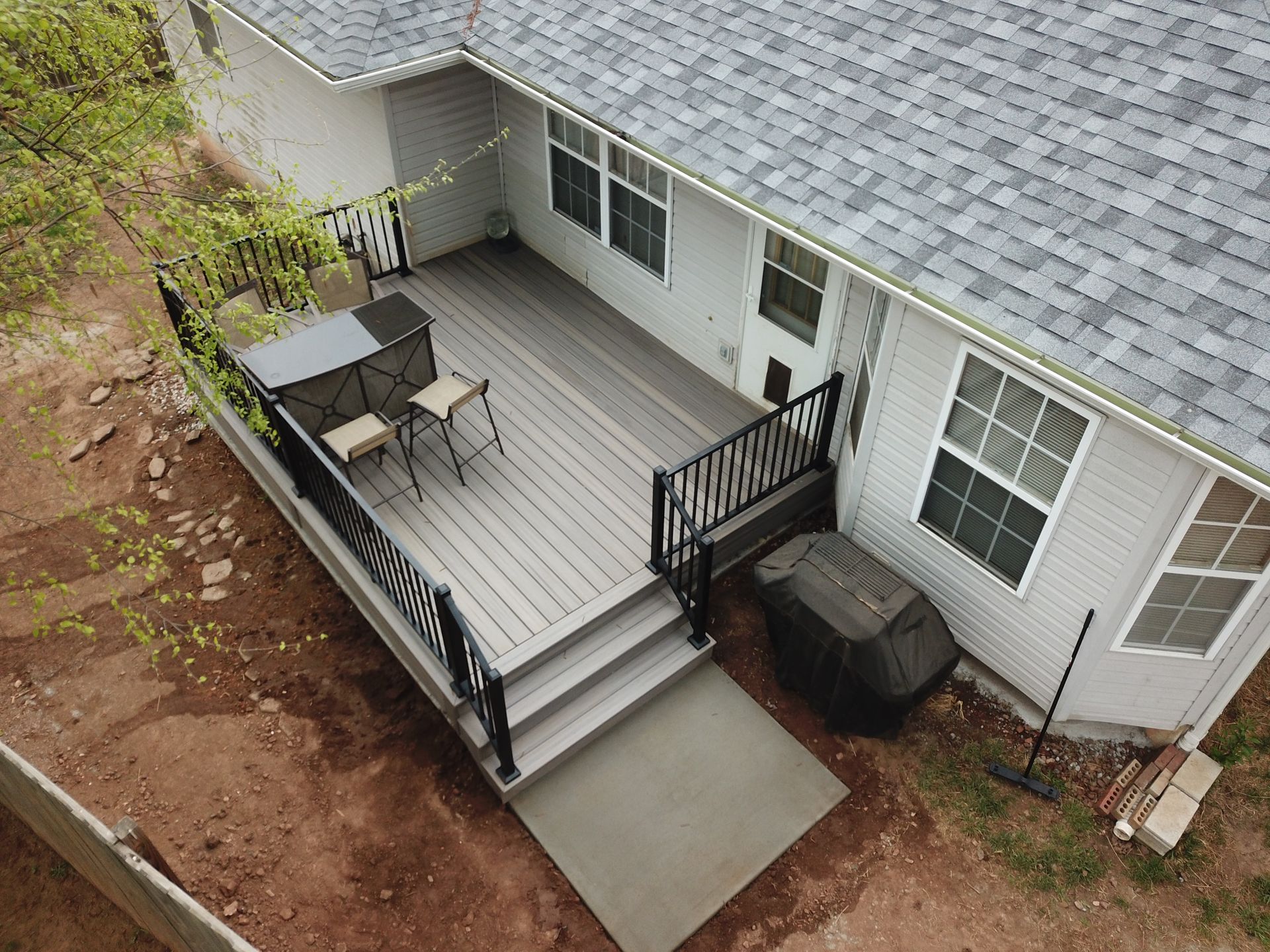 Back deck with stairs, black railings, patio table and chairs, and a grill beside the house