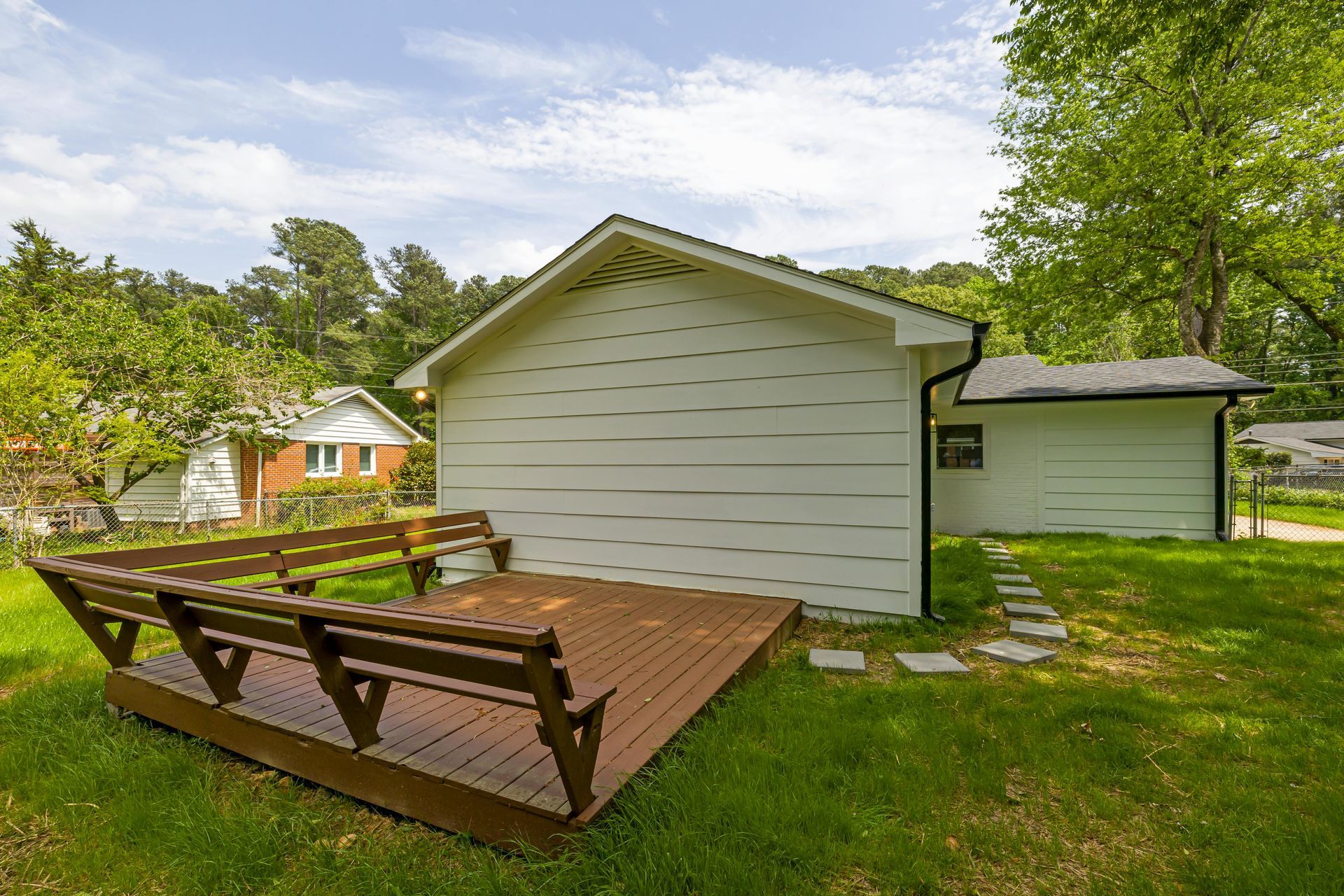 Patio with table and chairs beside a house, green hot tub, and pink lounge chairs under trees