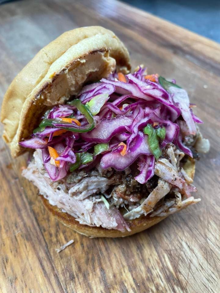 A pulled pork sandwich with coleslaw and carrots on a wooden cutting board.