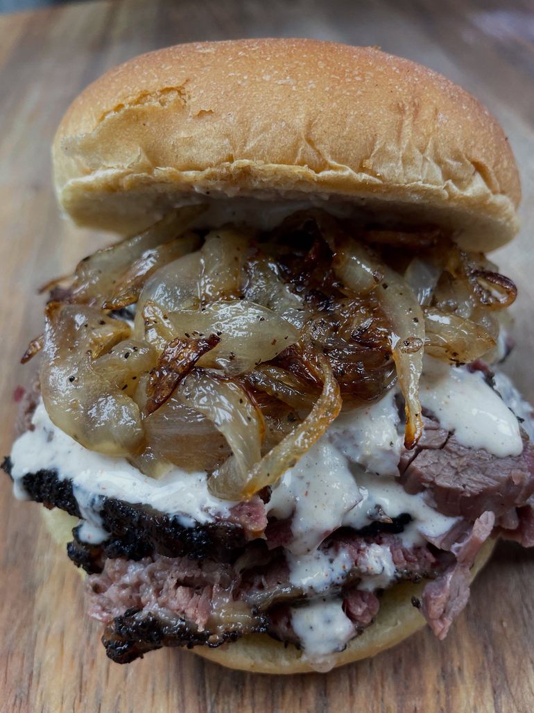 A sandwich with meat and onions on a bun on a wooden table.