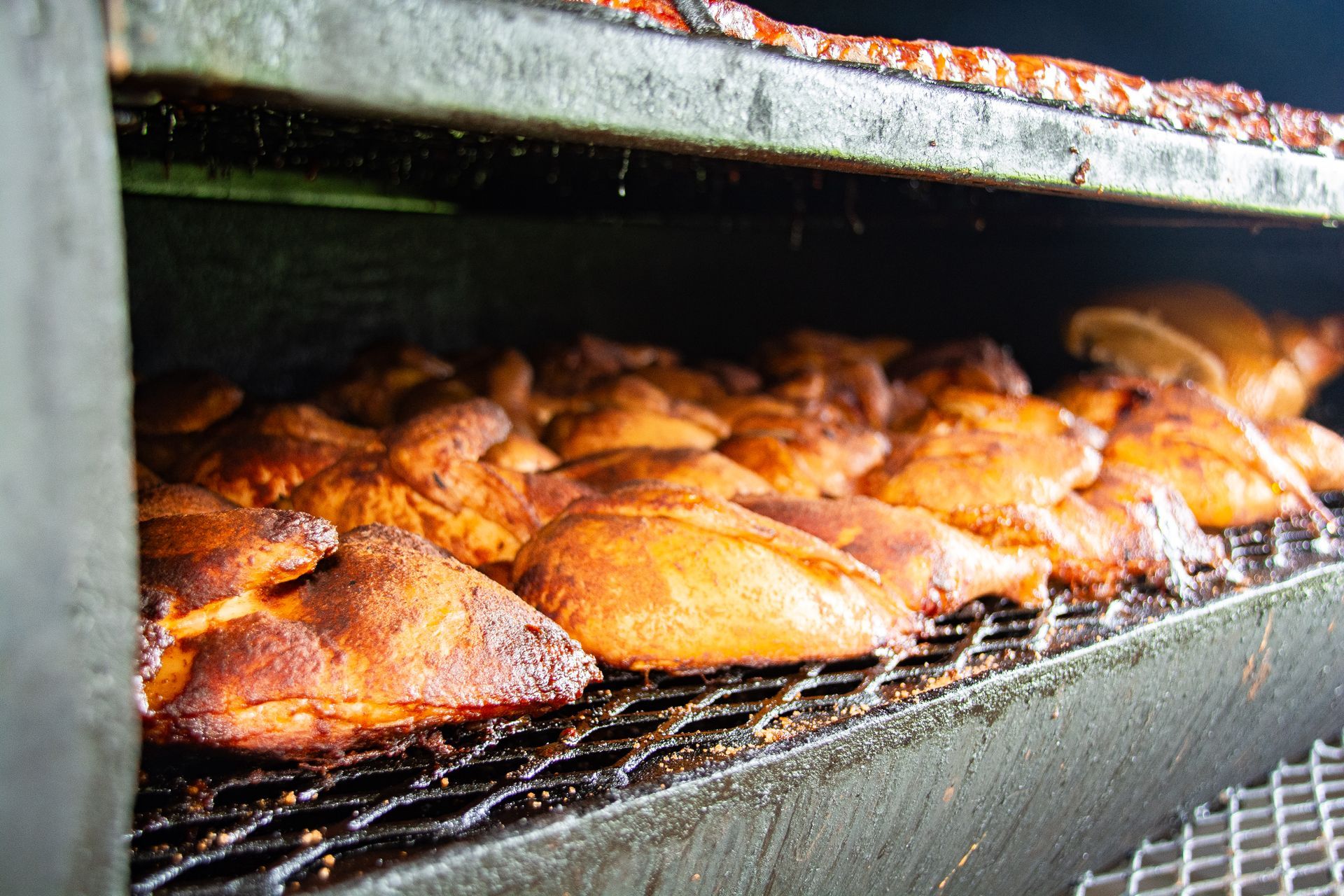 Smoked chicken pieces on a grill inside a black smoker. Brown, cooked meat.