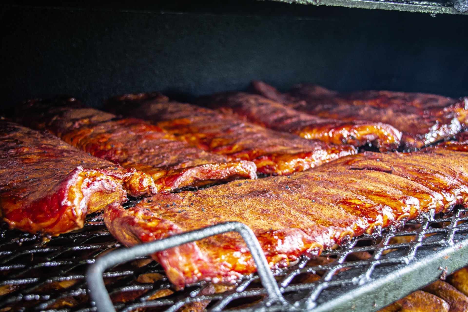 Smoked ribs on a grill, seasoned with a red-brown rub, inside a smoker.