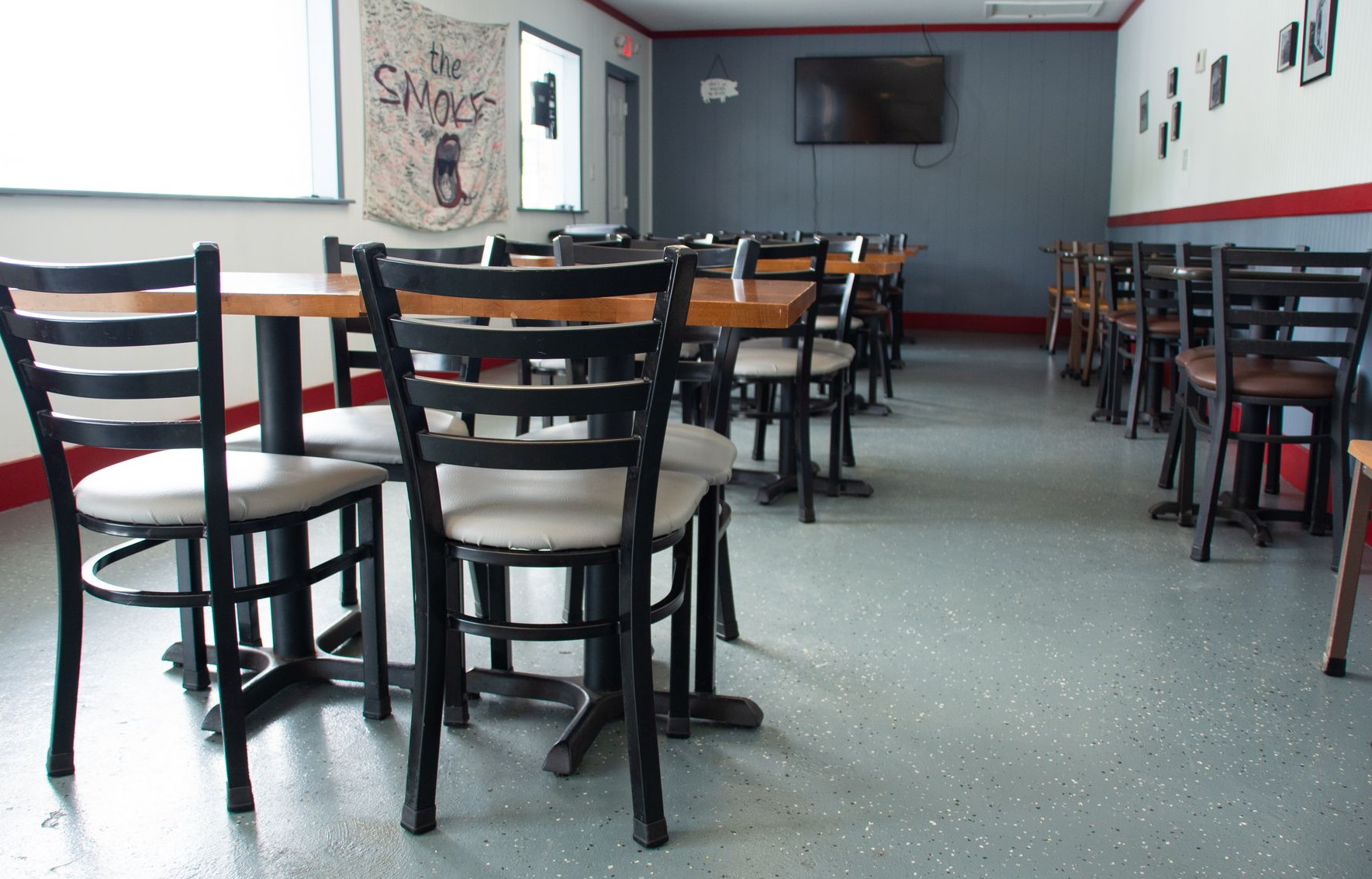 Empty restaurant interior with tables and chairs. Gray floor, red and gray walls, and a TV.