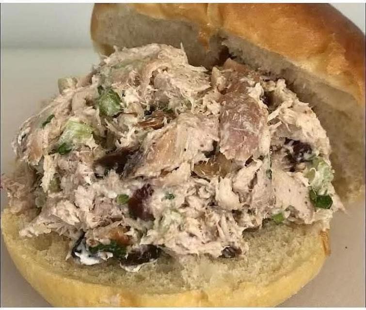 A styrofoam container filled with meat , beans , macaroni and cheese , and pickles.