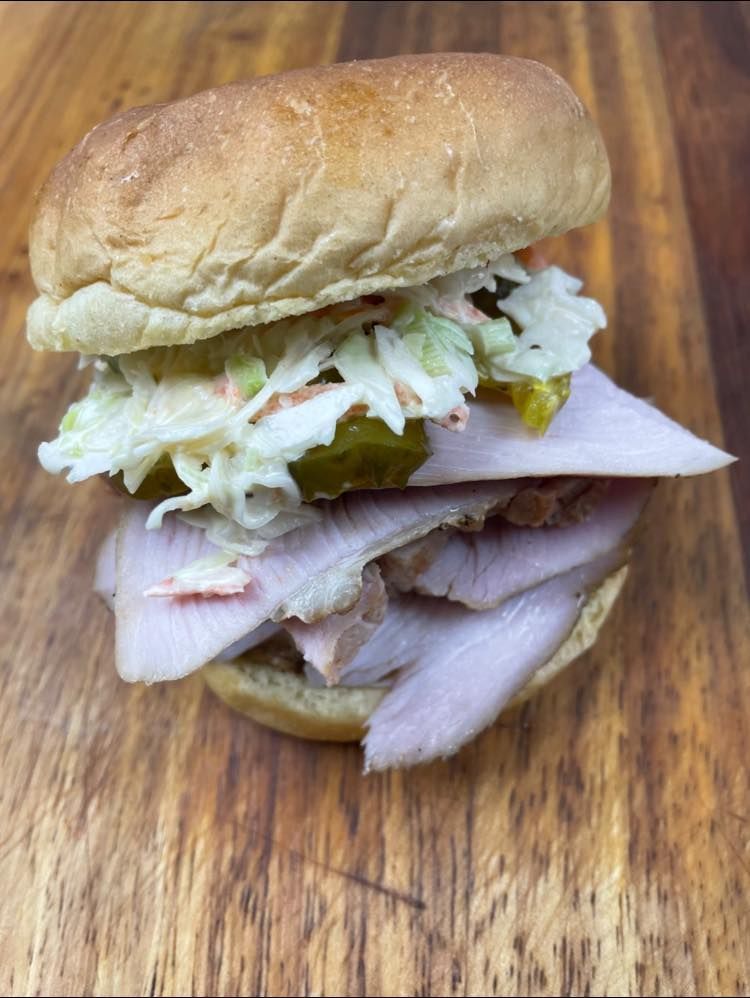A pulled pork sandwich with coleslaw and carrots on a wooden cutting board.