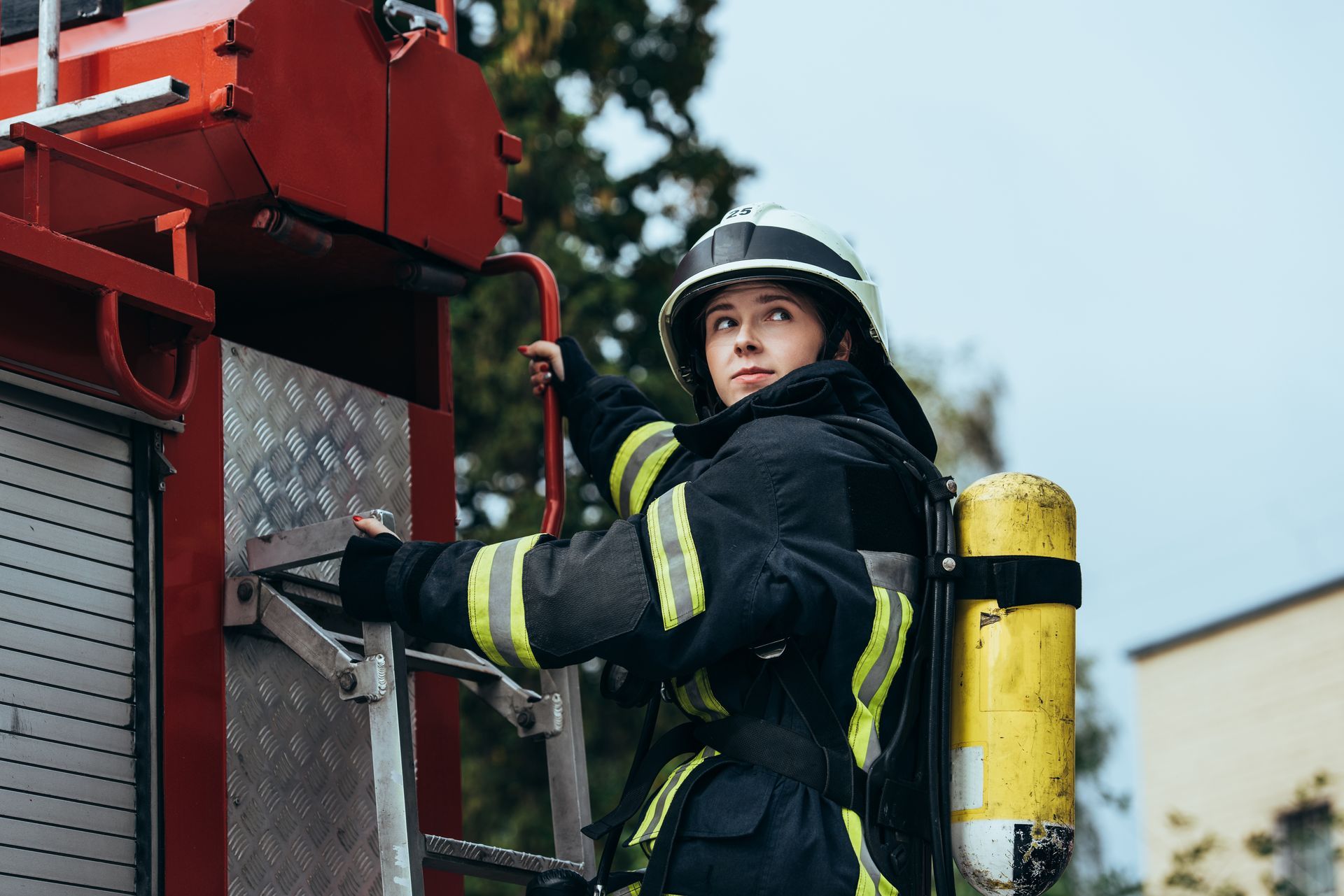 Firefighter adjusting helmet in front of firetruck in a station.