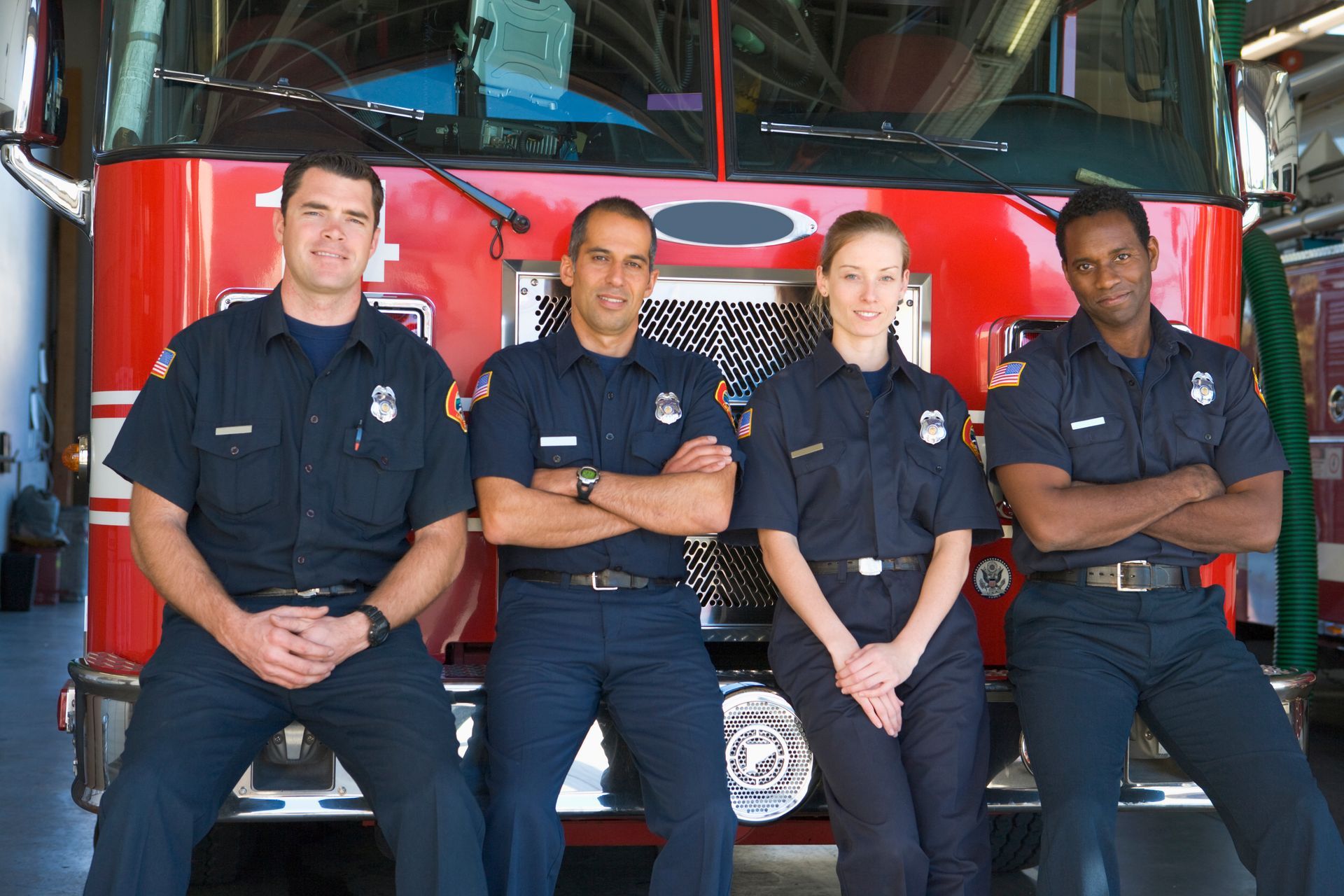 Firefighter in uniform, red fire extinguisher, standing near a fire truck inside a station.
