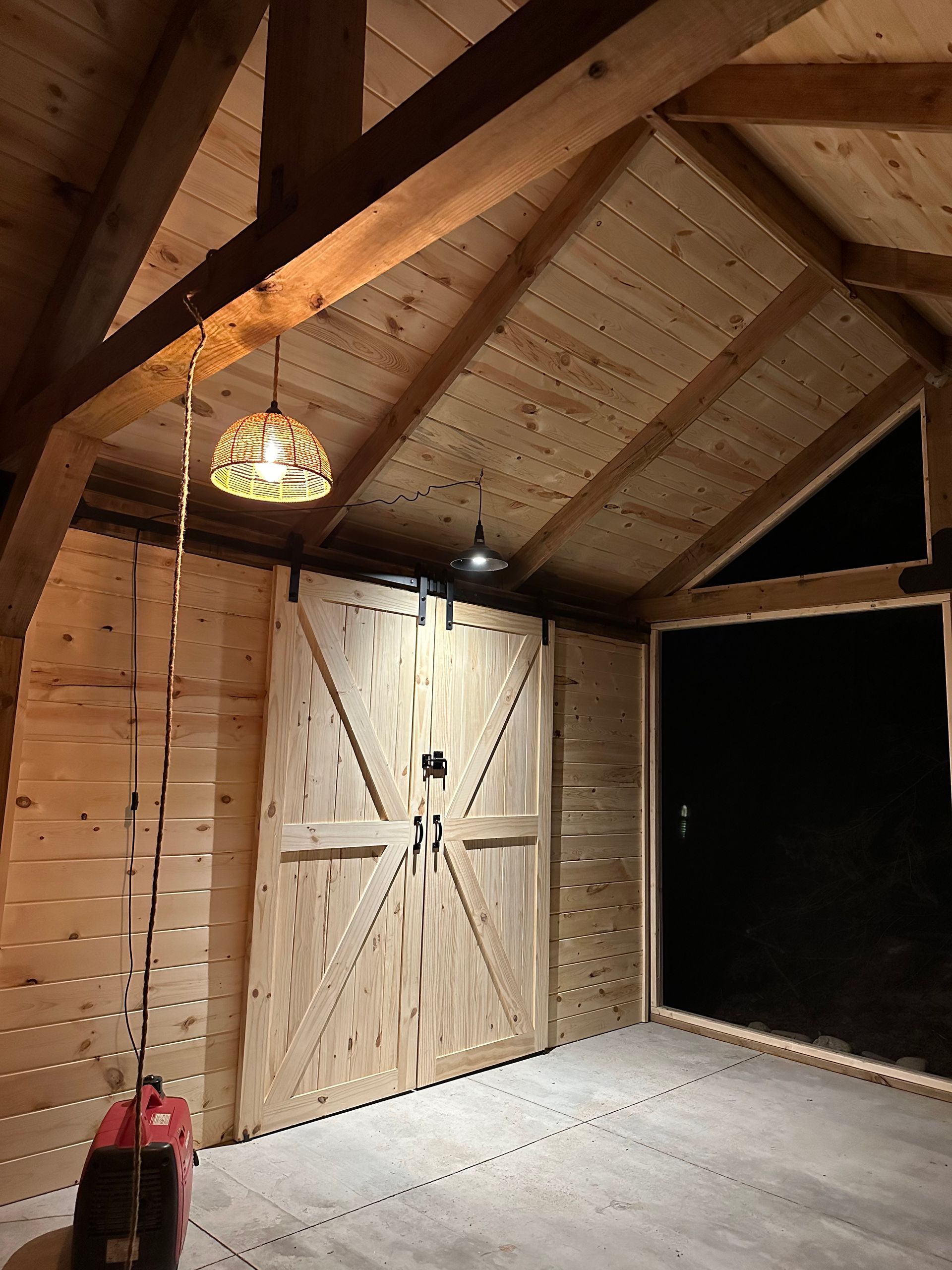 A wooden garage with a large wooden door and a lamp hanging from the ceiling.