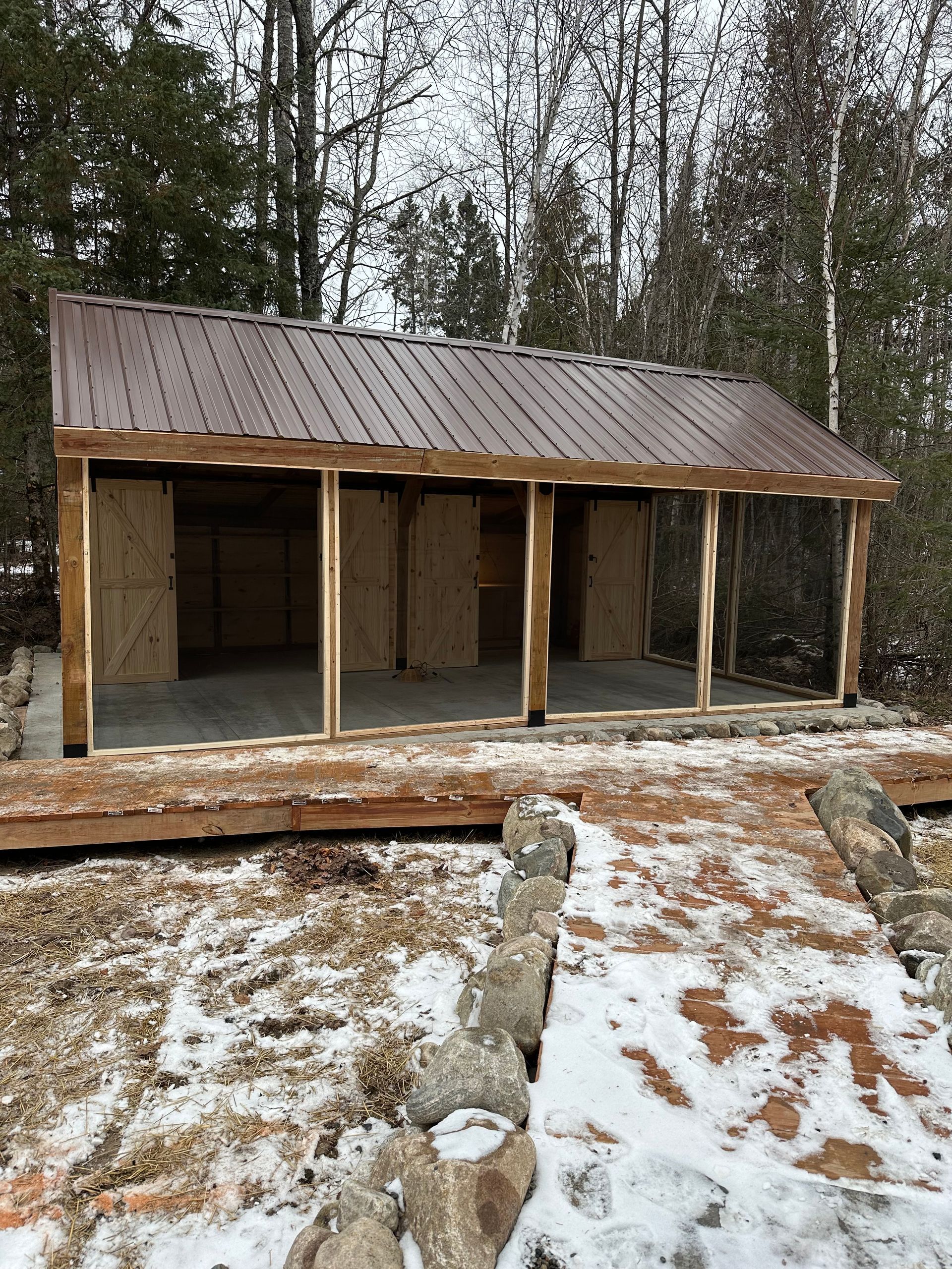 A wooden shed with a metal roof is being built in the woods.