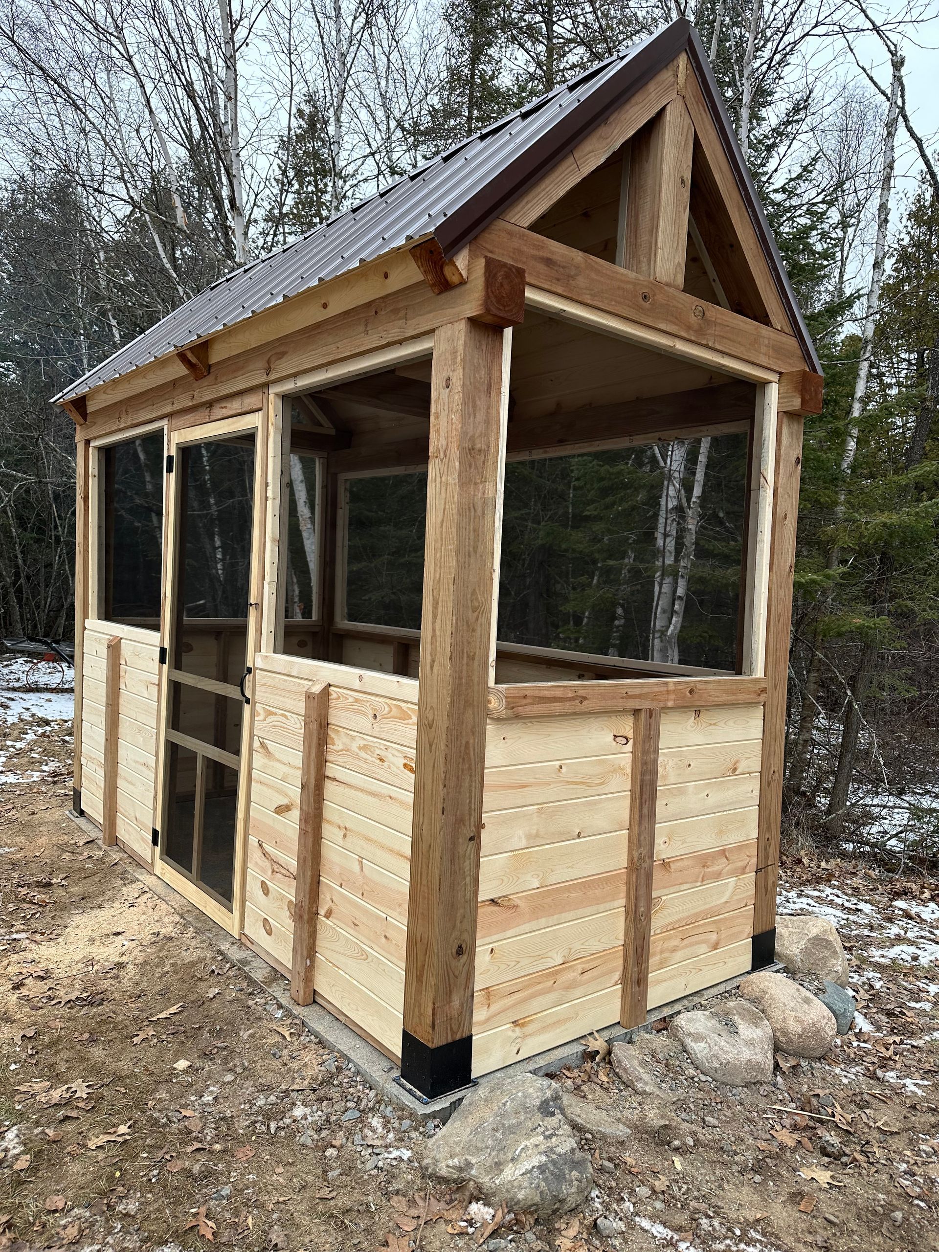 A wooden shed with a screened in porch in the woods.