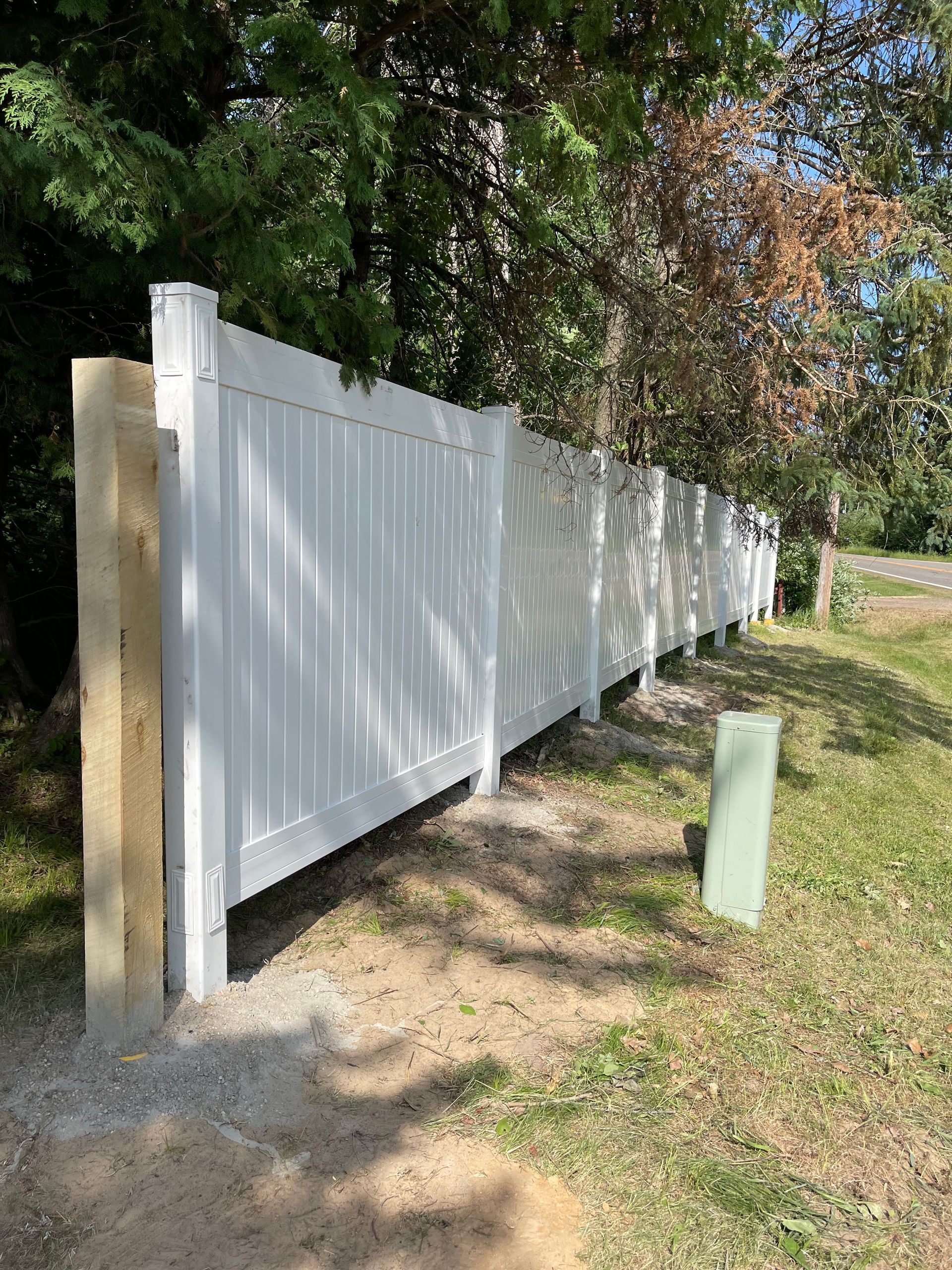 A white vinyl fence is surrounded by trees and grass.