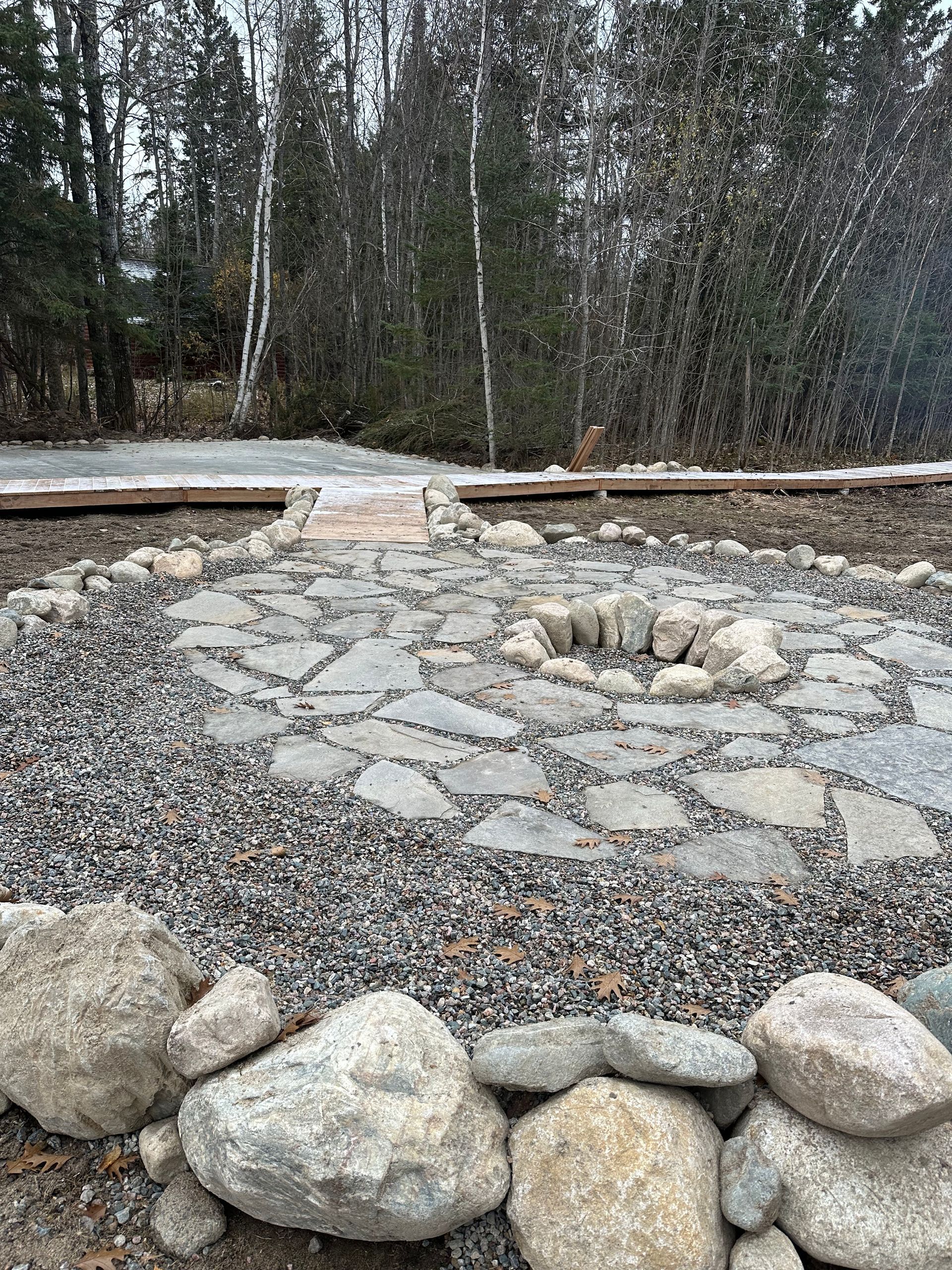 A fire pit is surrounded by rocks and gravel in the middle of a forest.