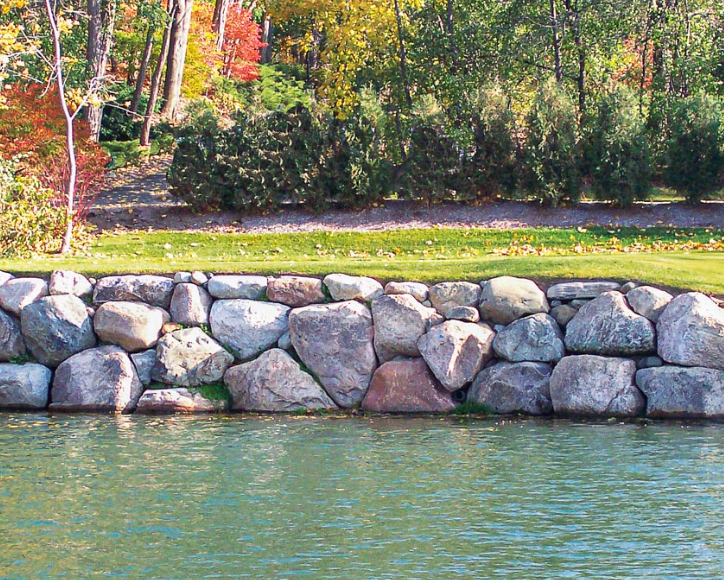 Stone retaining wall on the edge of a body of water with trees in the background.