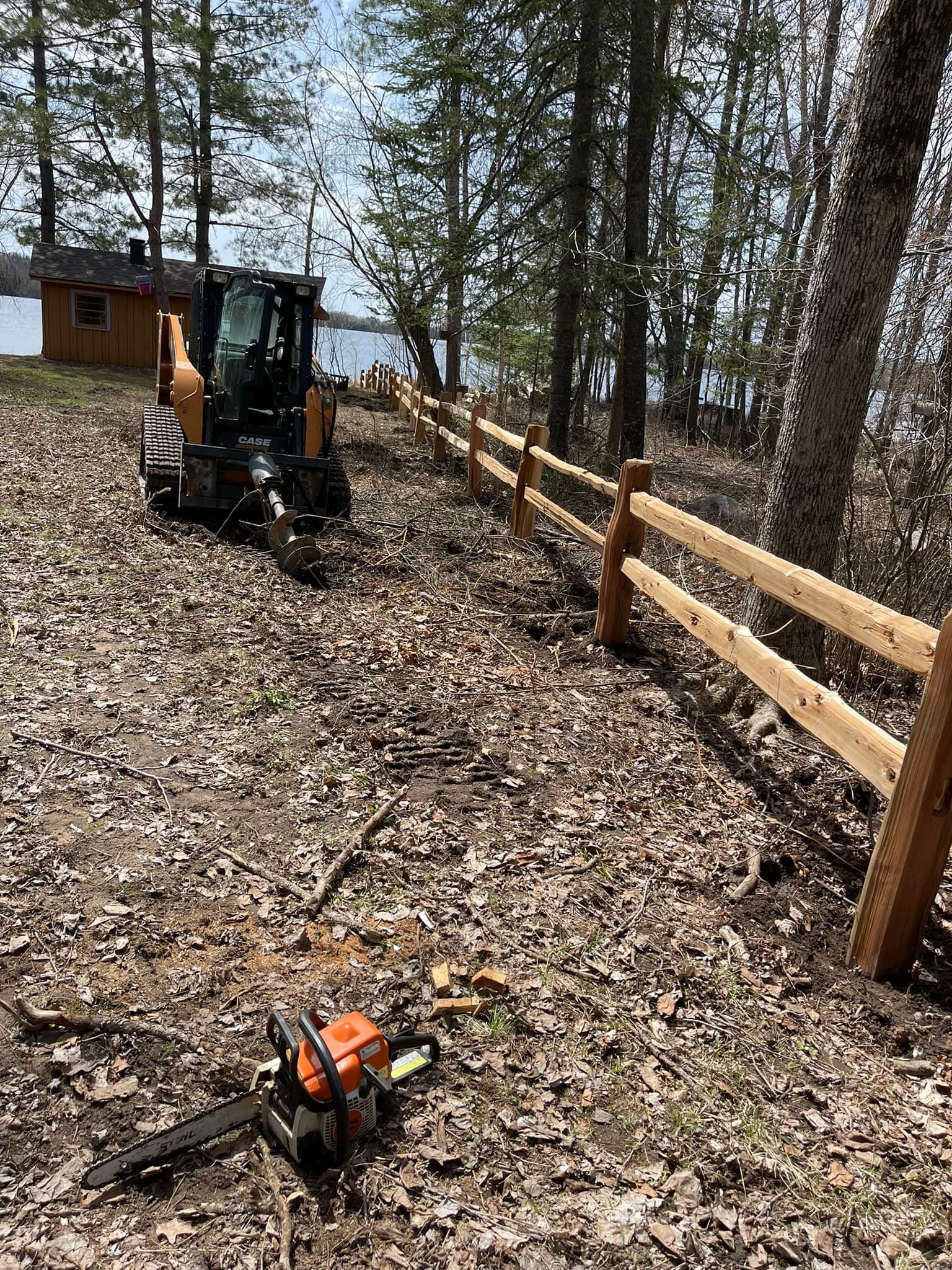 A chainsaw is sitting on the ground next to a wooden fence.