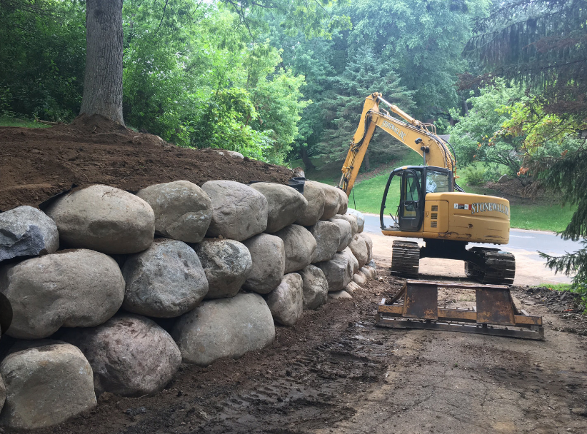 A yellow excavator is working on a rock wall.