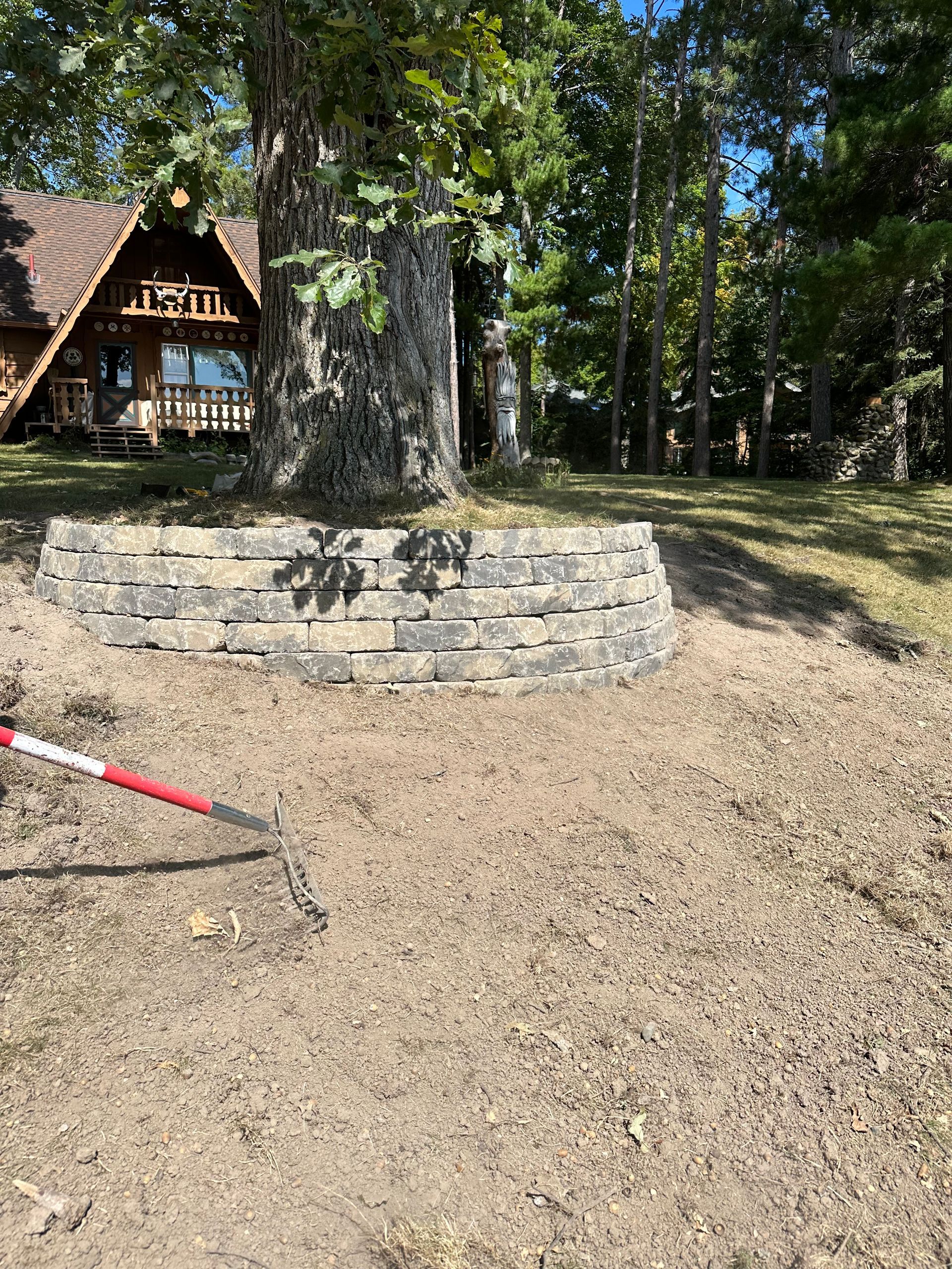 A person is raking dirt in a yard in front of a house.