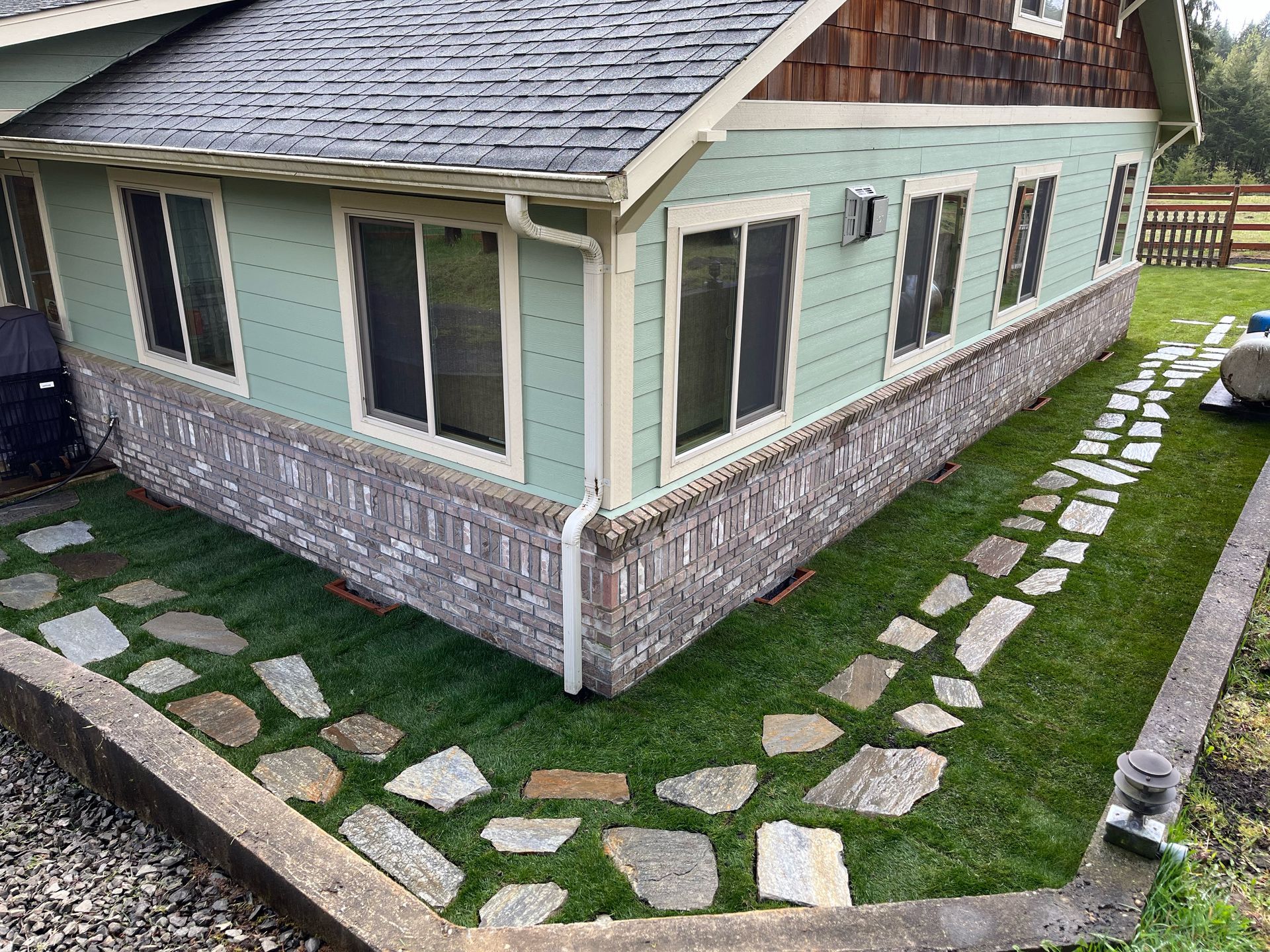 House with green siding and brick base, stone path on turf lawn.