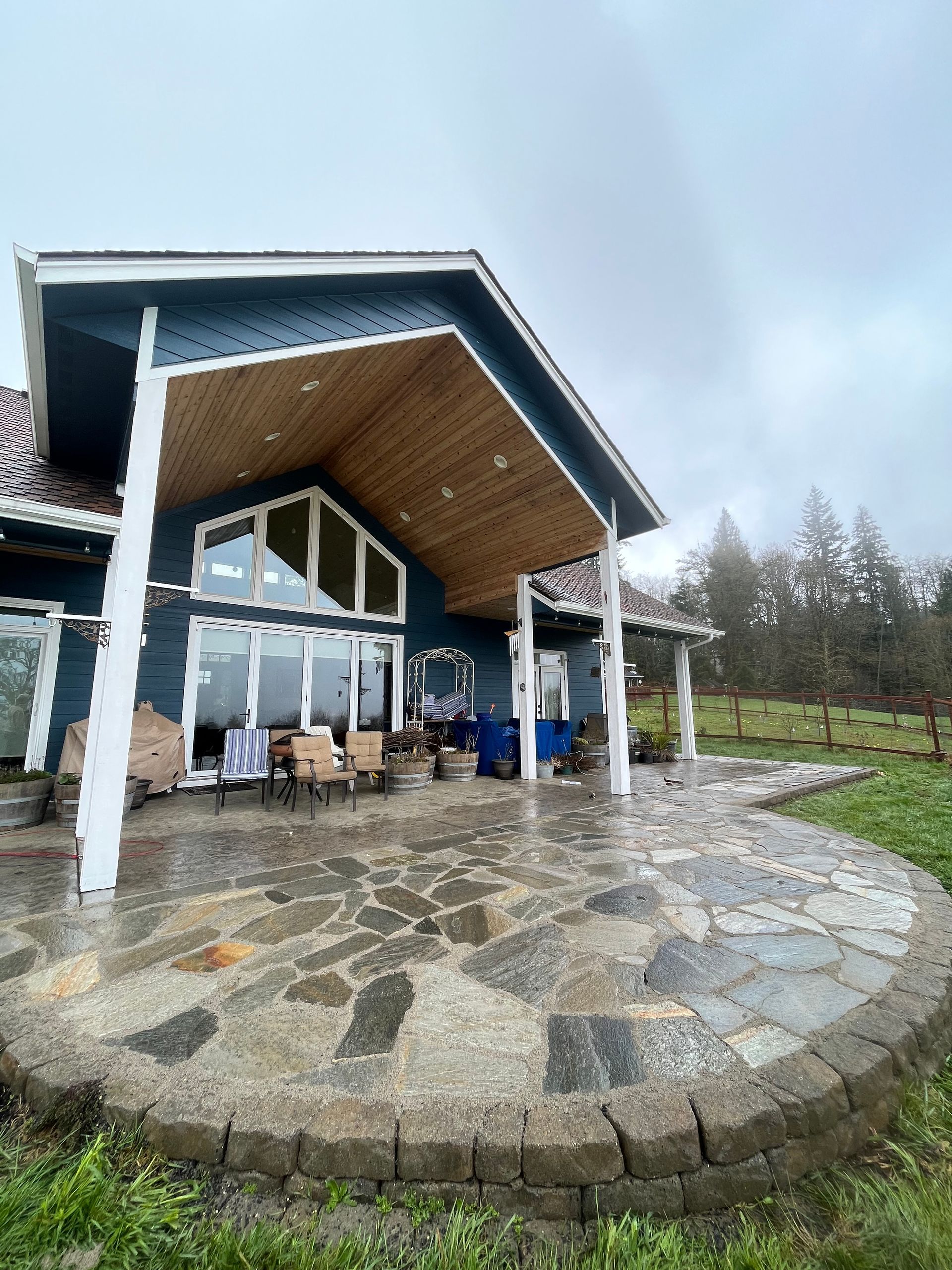 Blue house with large patio under a wooden covered area on a cloudy day.