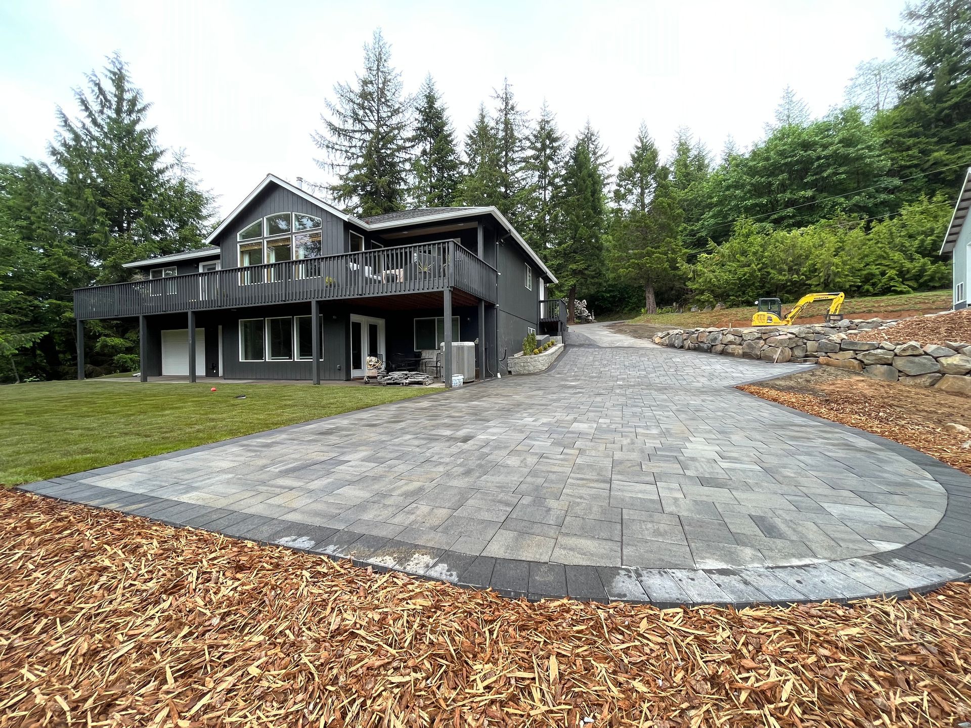 Gray house with a paved driveway on a wooded hillside.