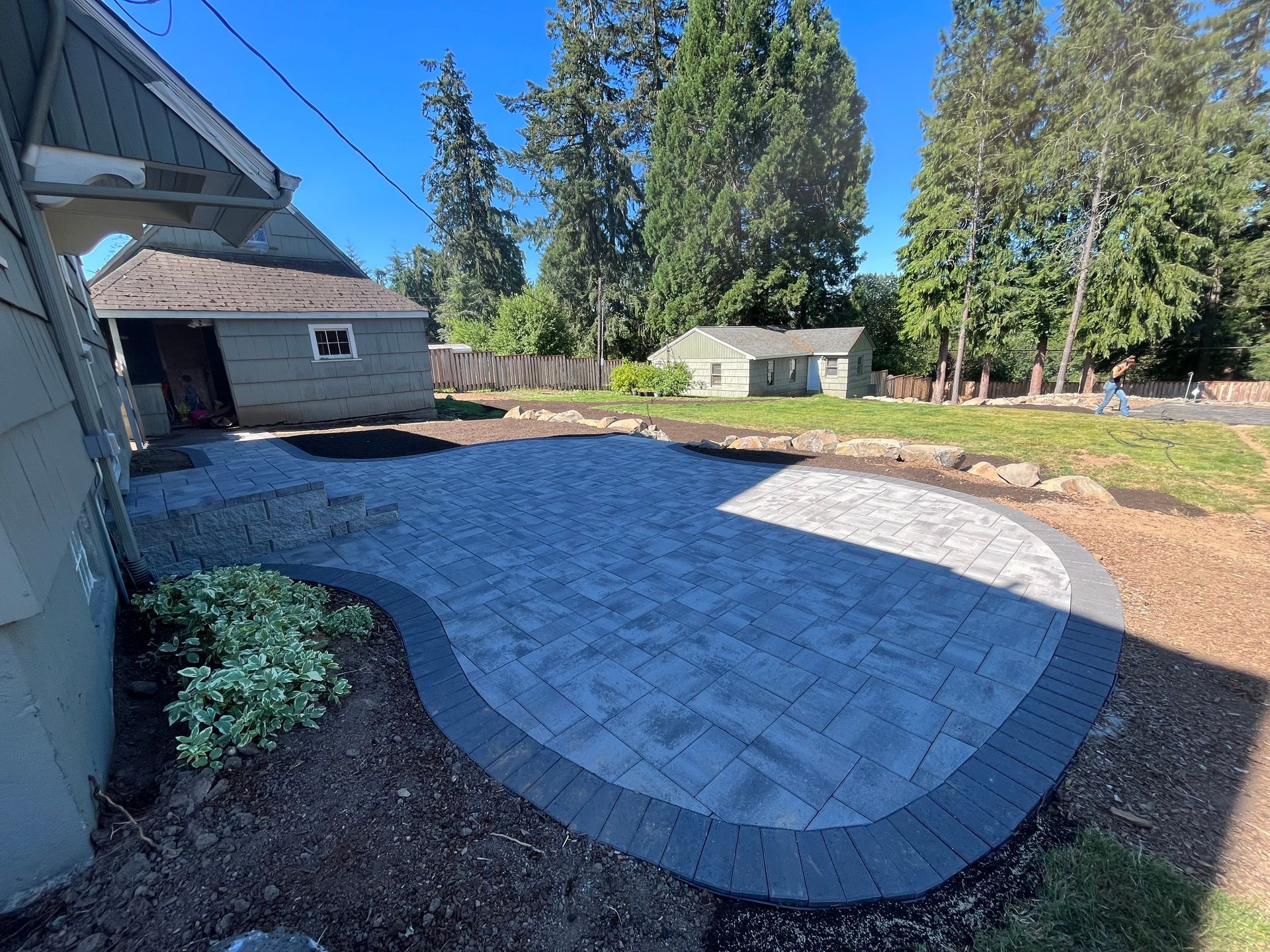 A newly paved gray patio with a dark border in a backyard setting.
