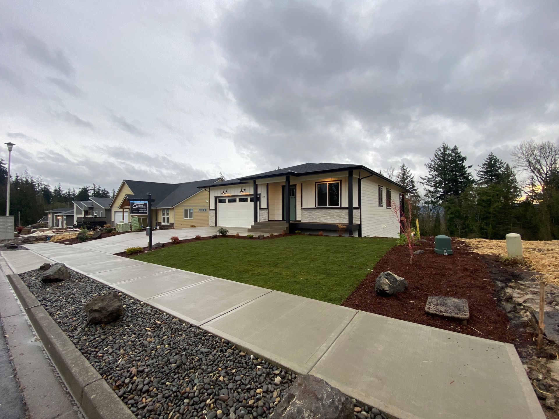 A new, beige single-story house with black accents and a well-manicured lawn on a cloudy day.