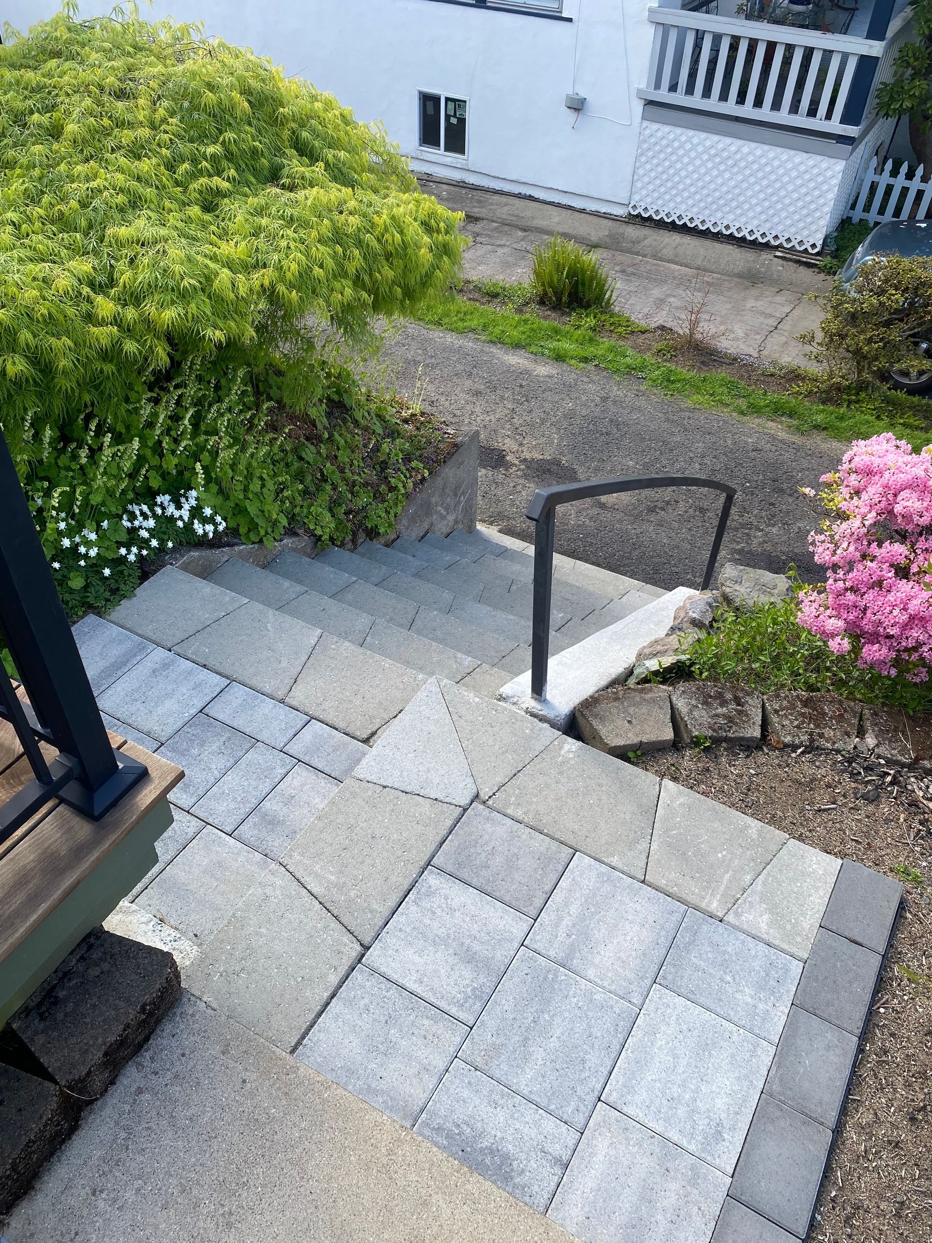 Stone steps with a handrail leading up to a house surrounded by greenery and flowers.