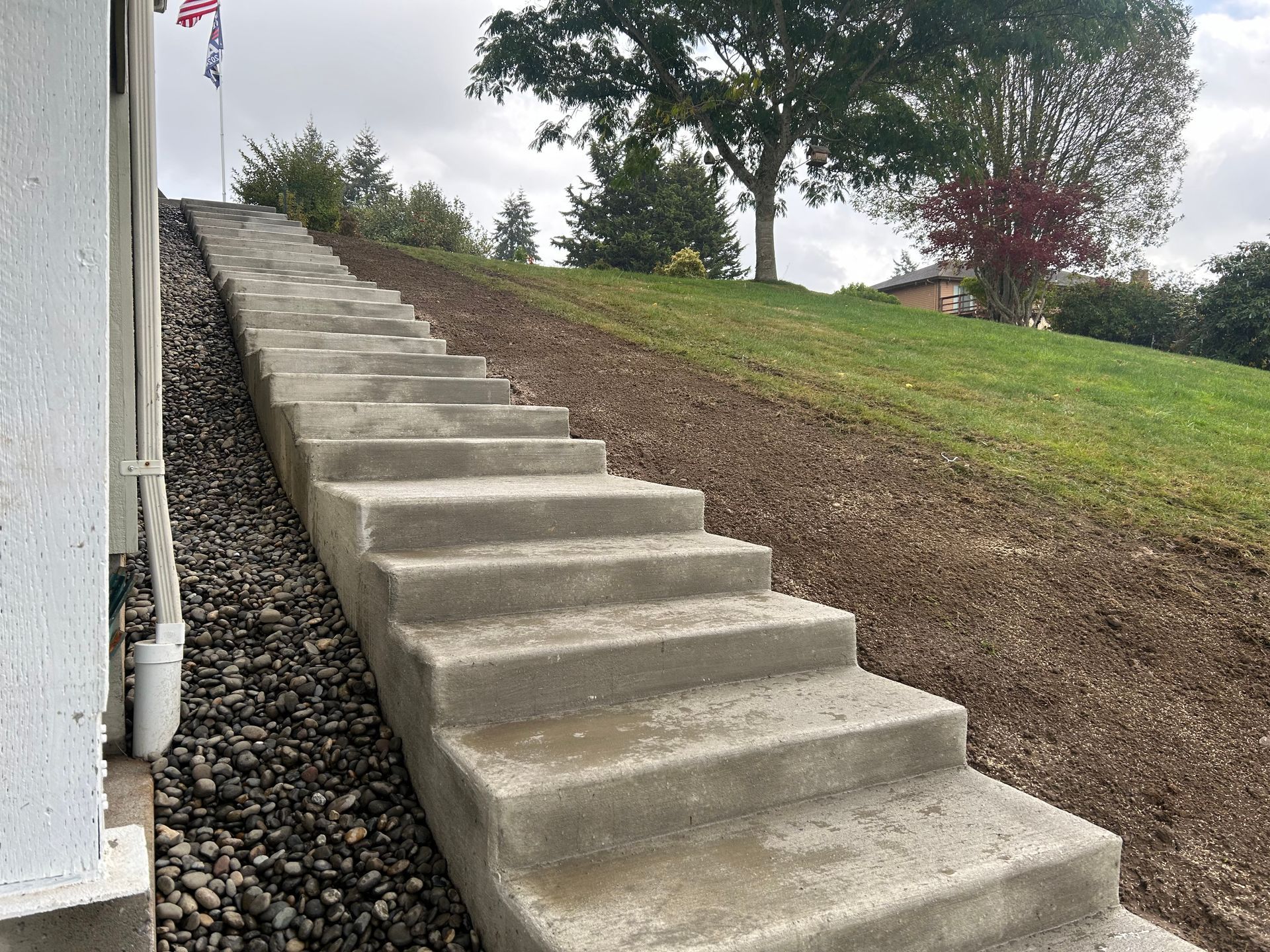 Concrete stairs ascending a grassy hill. Gravel on the left, trees and flags in the background.