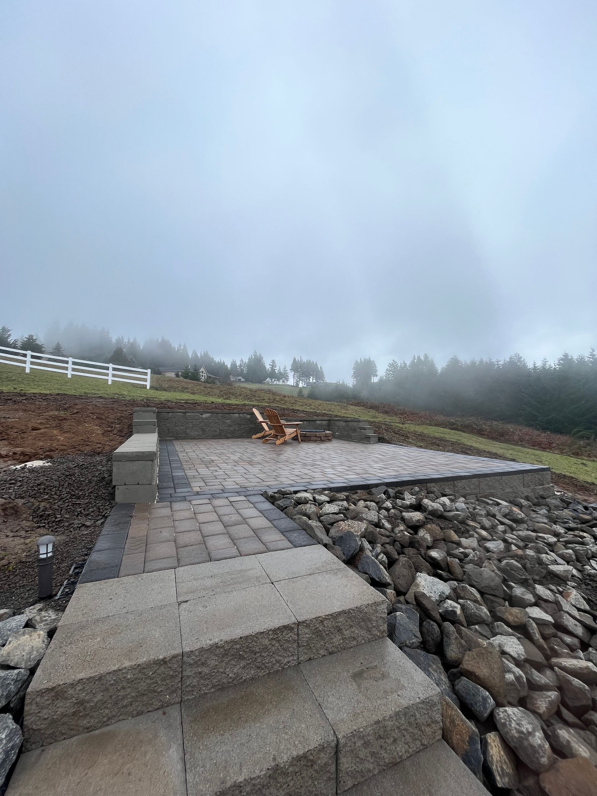 Stone patio with steps, rock wall, and foggy hillside.