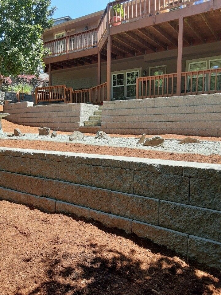 Exterior view of a house with tiered retaining walls made of gray blocks and a wooden deck.