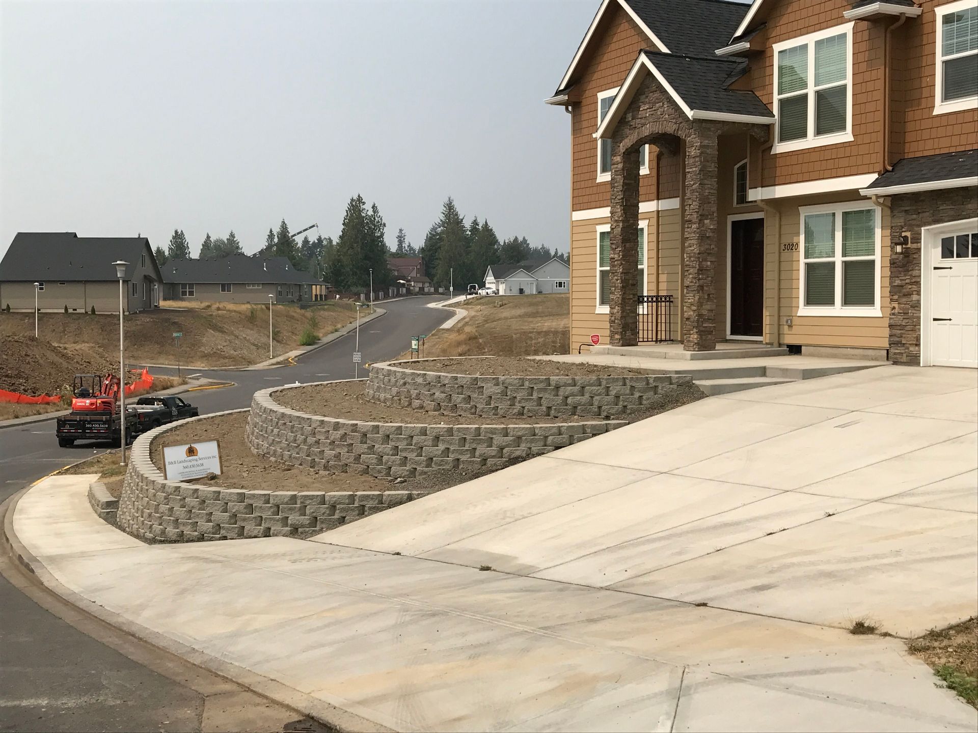 New home with tiered retaining walls along a sloped driveway on a street under construction.