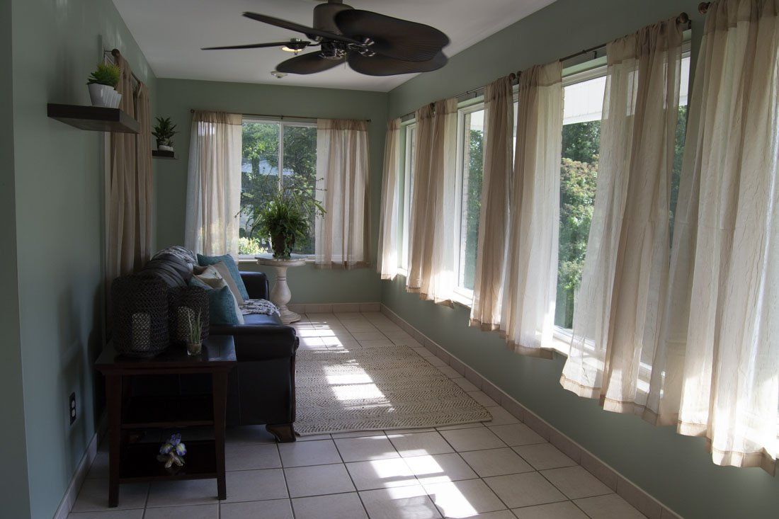 A living room with a ceiling fan and lots of windows