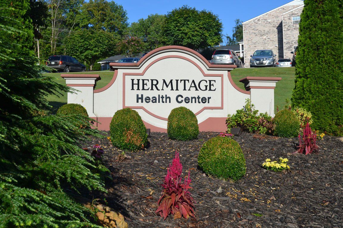 A sign for hermitage health center is surrounded by bushes and flowers