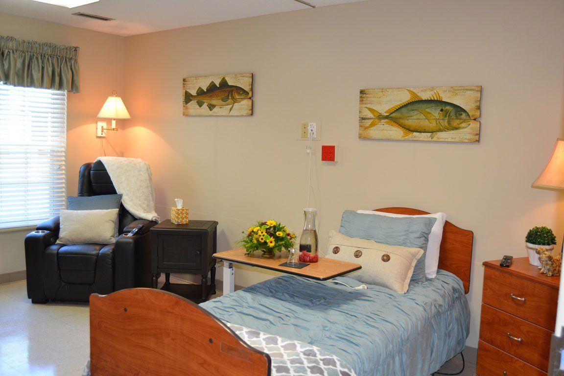 A bedroom with a bed , chair , nightstand , lamp and paintings on the wall.