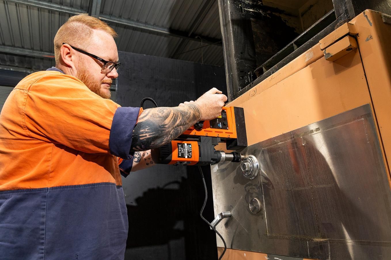 Man Using a Magnetic Drill on a Metal Surface, Wearing Safety Glasses and Work Clothes — Active 24/7 Locksmith and Security Services in Forster, NSW