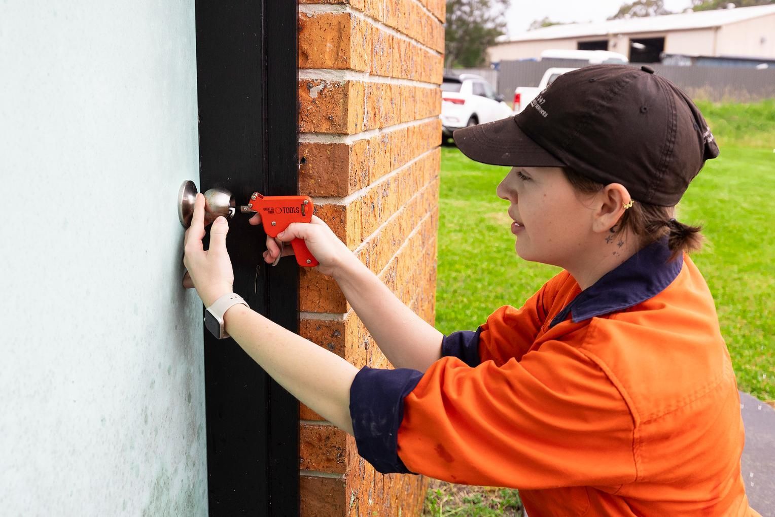 Woman in Orange Shirt Installing a Door Handle on a Brick Building — Active 24/7 Locksmith and Security Services in Forster, NSW