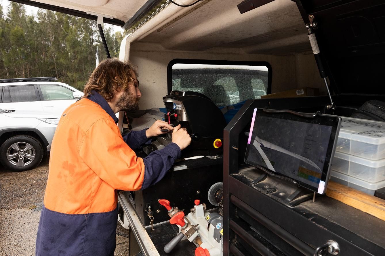A Locksmith in an Orange Work Jacket Working on a Key Cutting Machine Inside a Van — Active 24/7 Locksmith and Security Services in Forster, NSW