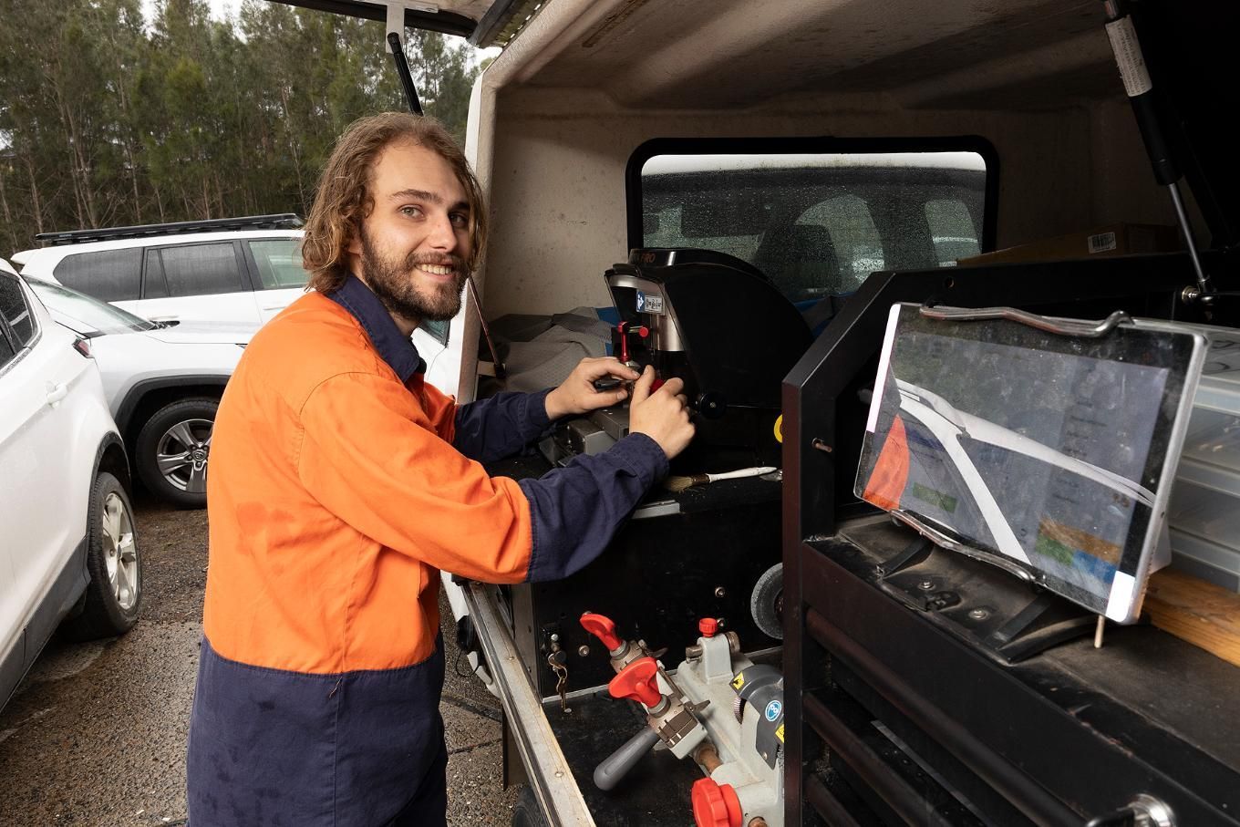 Man in Orange Work Shirt Works on Equipment in the Back of a Utility Truck; a Tablet Displays a Map — Active 24/7 Locksmith and Security Services in Taree, NSW