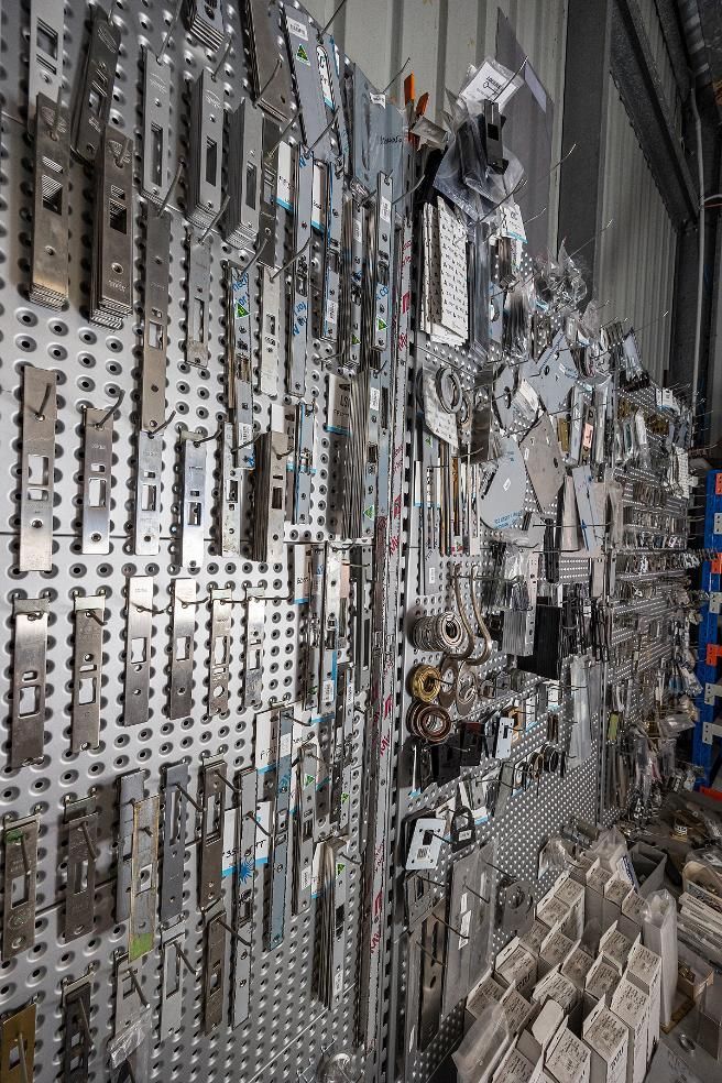 Metal Hardware Components, Mostly Door Latches, Displayed on a Perforated Metal Wall — Active 24/7 Locksmith and Security Services in Forster, NSW