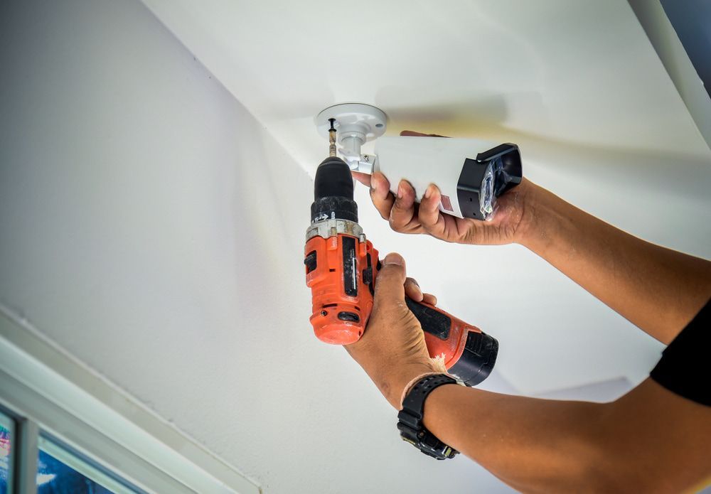 A Person Is Using a Drill to Install a Security Camera on The Ceiling — Active 24/7 Locksmiths Forster In Taree, NSW