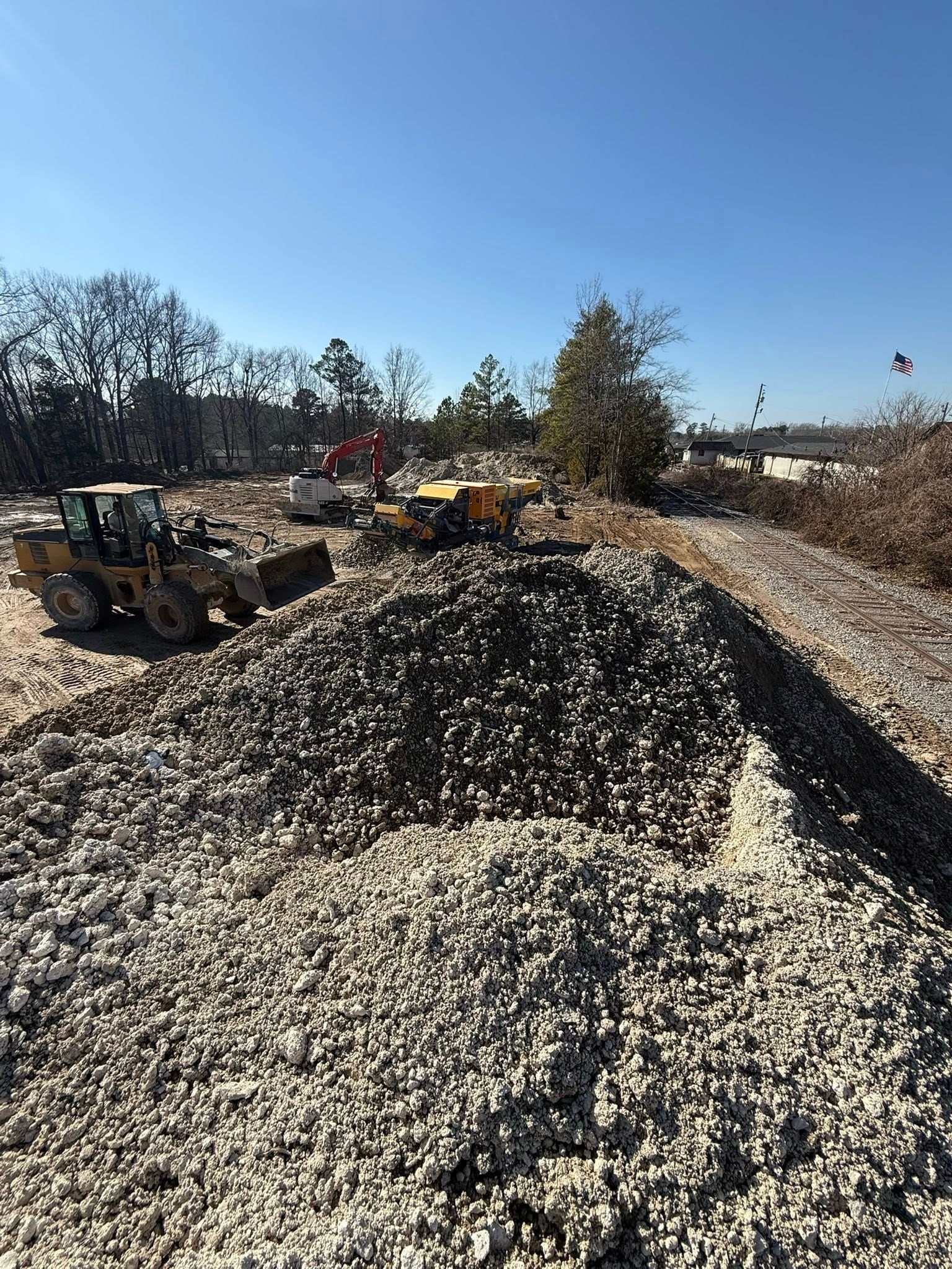Heavy machinery clears a large pile of rocks and debris at a construction site under a clear blue sky.