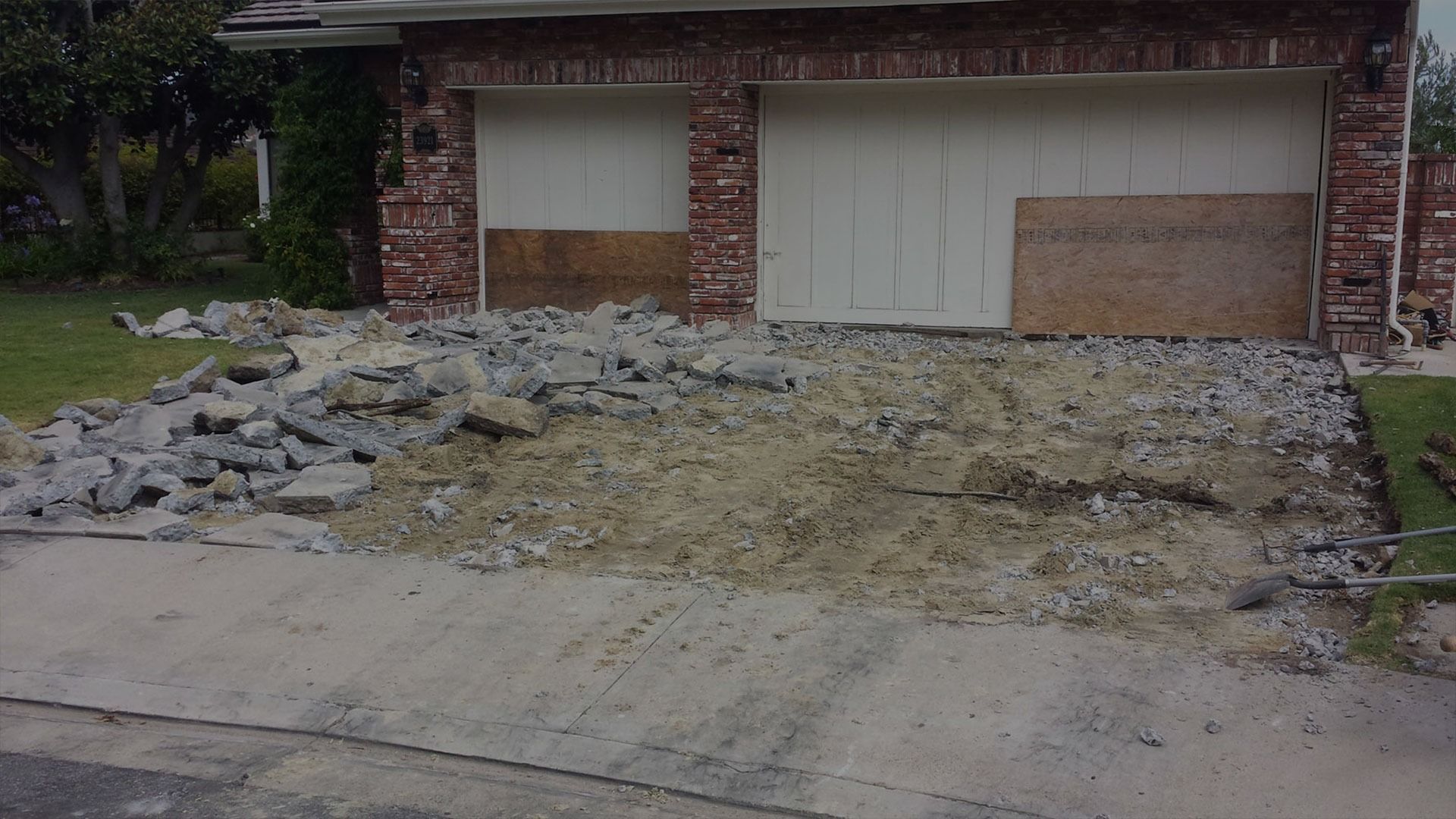 A house with a dirt and rubble-covered driveway in front of the garage doors.