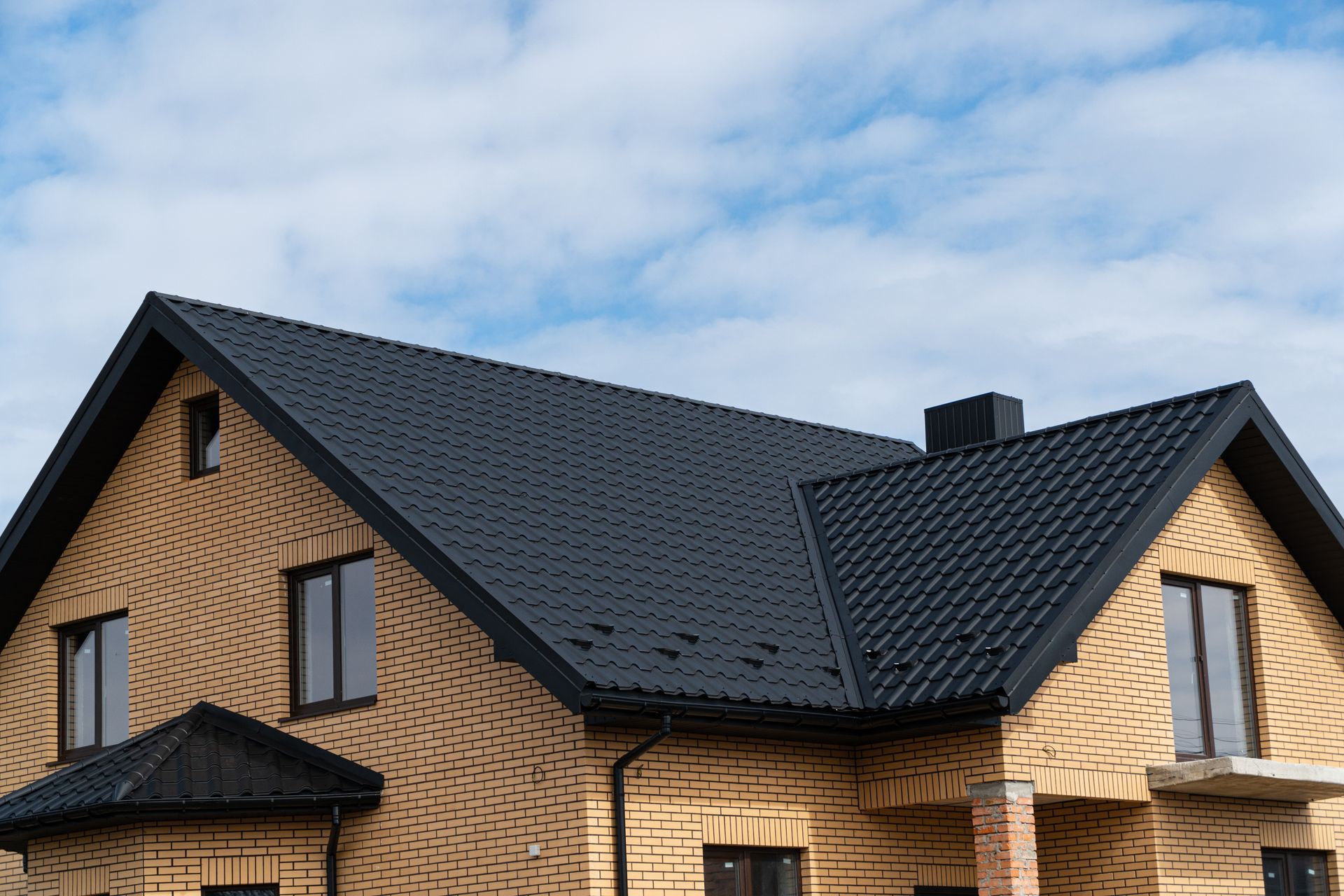 A brick house with a black roof and windows.